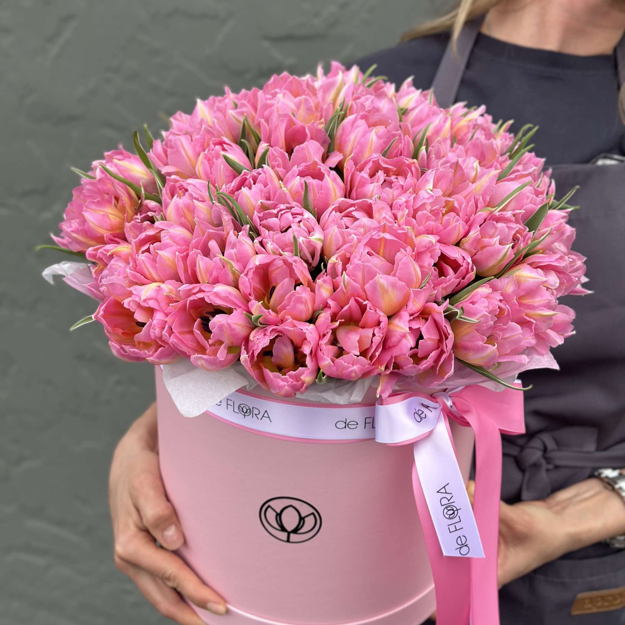 Pink tulips arranged in a round pink hat box with a ribbon