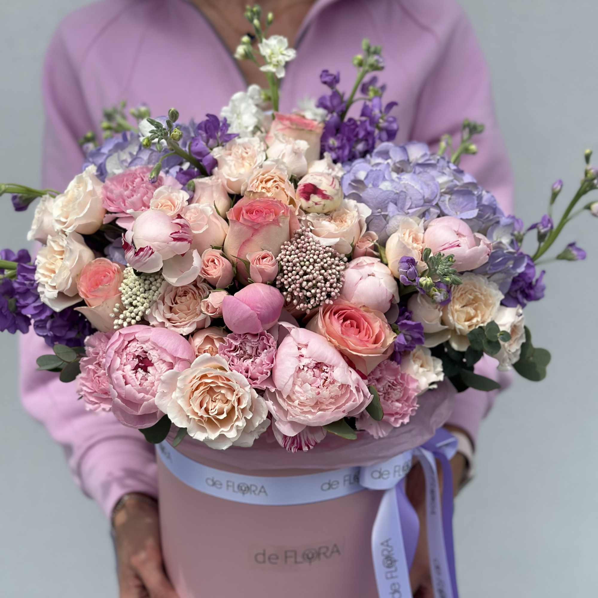 Large pastel bouquet of pink, peach, white, and purple flowers in a pink hat box