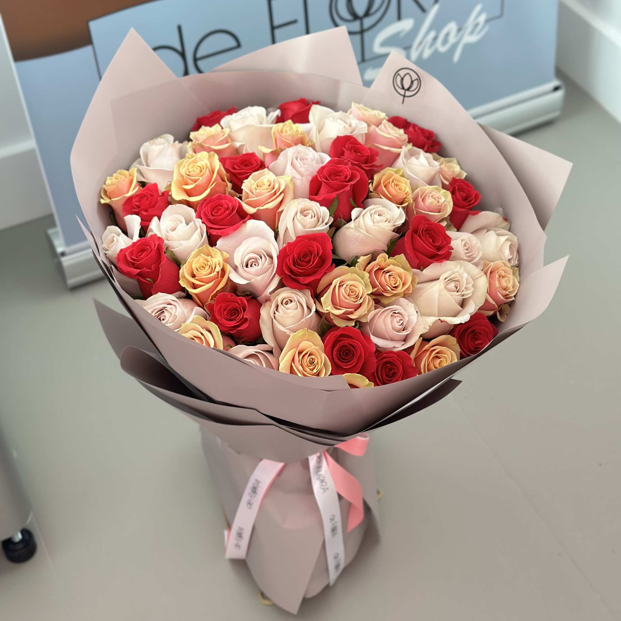 Large bouquet of red, blush, and peach roses wrapped in pale paper