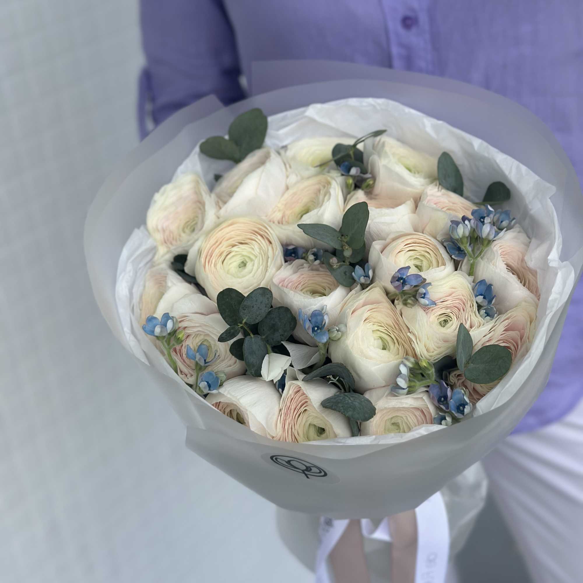 Bouquet of pale ranunculus with blue accents wrapped in white paper