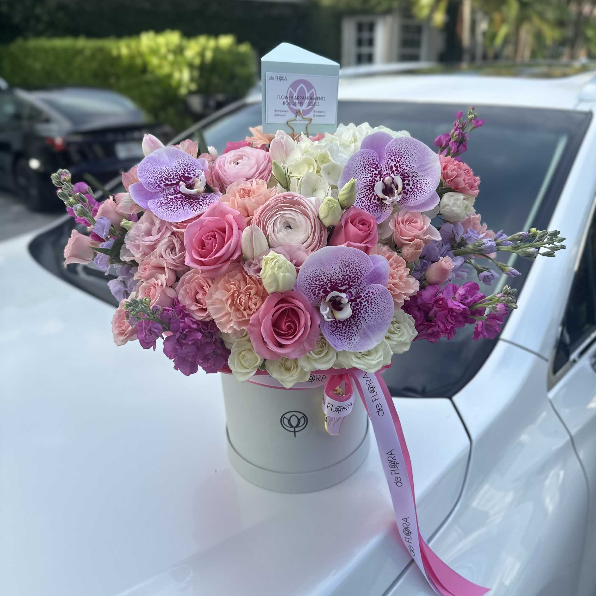 Pastel pink and lavender flower arrangement with orchids and roses in a white hat box.