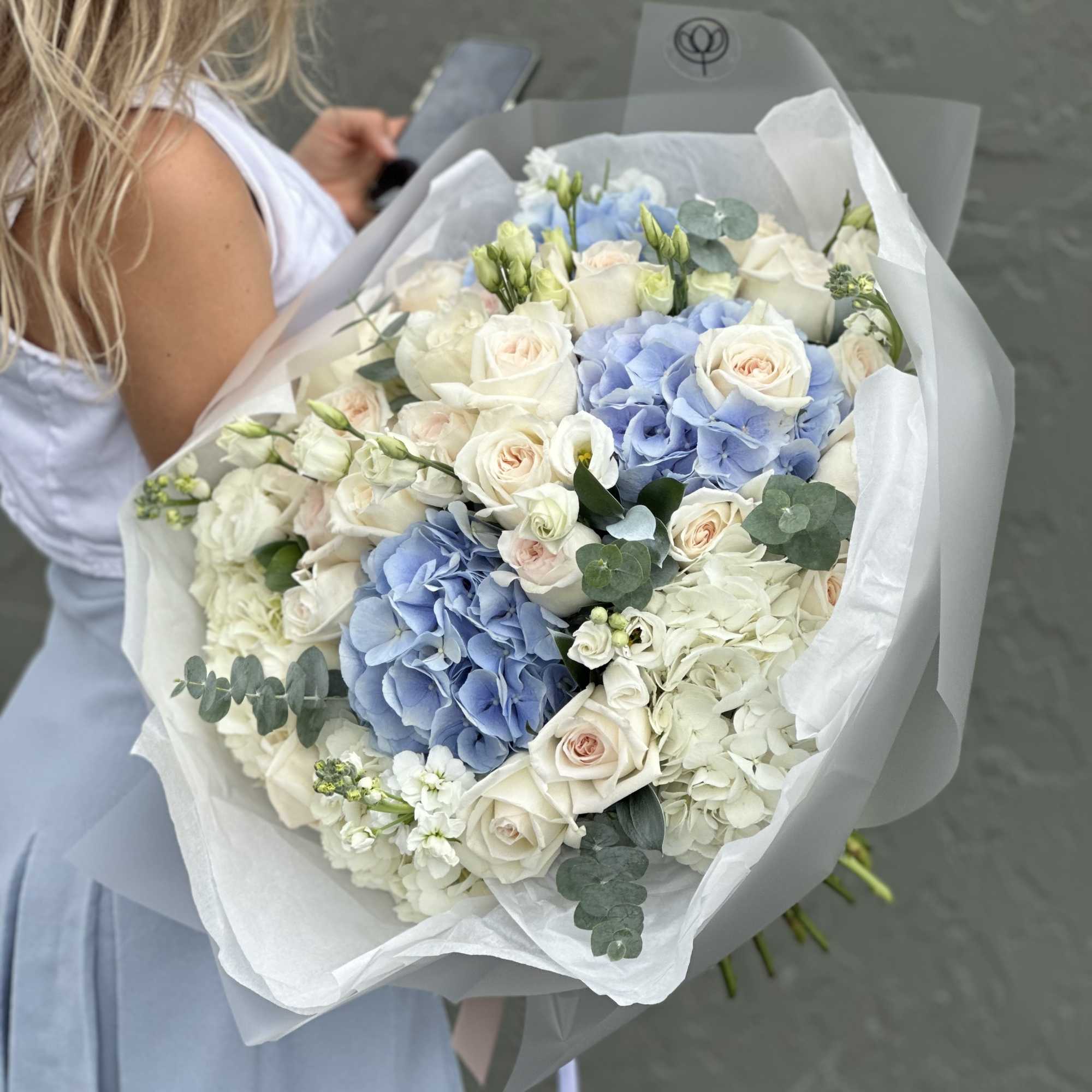 Large bouquet of white roses and blue hydrangeas wrapped in white paper