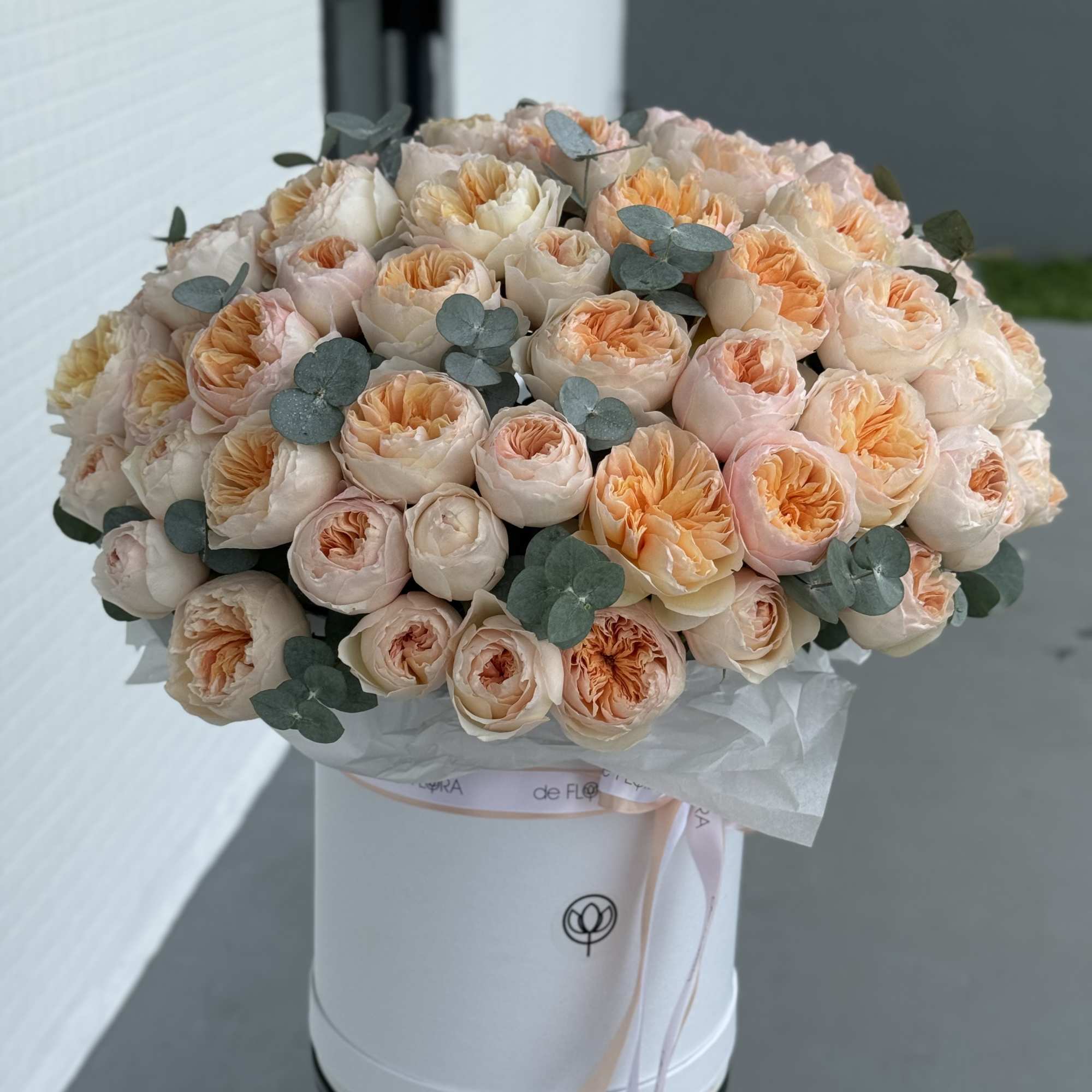 Peach and blush roses arranged in a white hatbox with eucalyptus