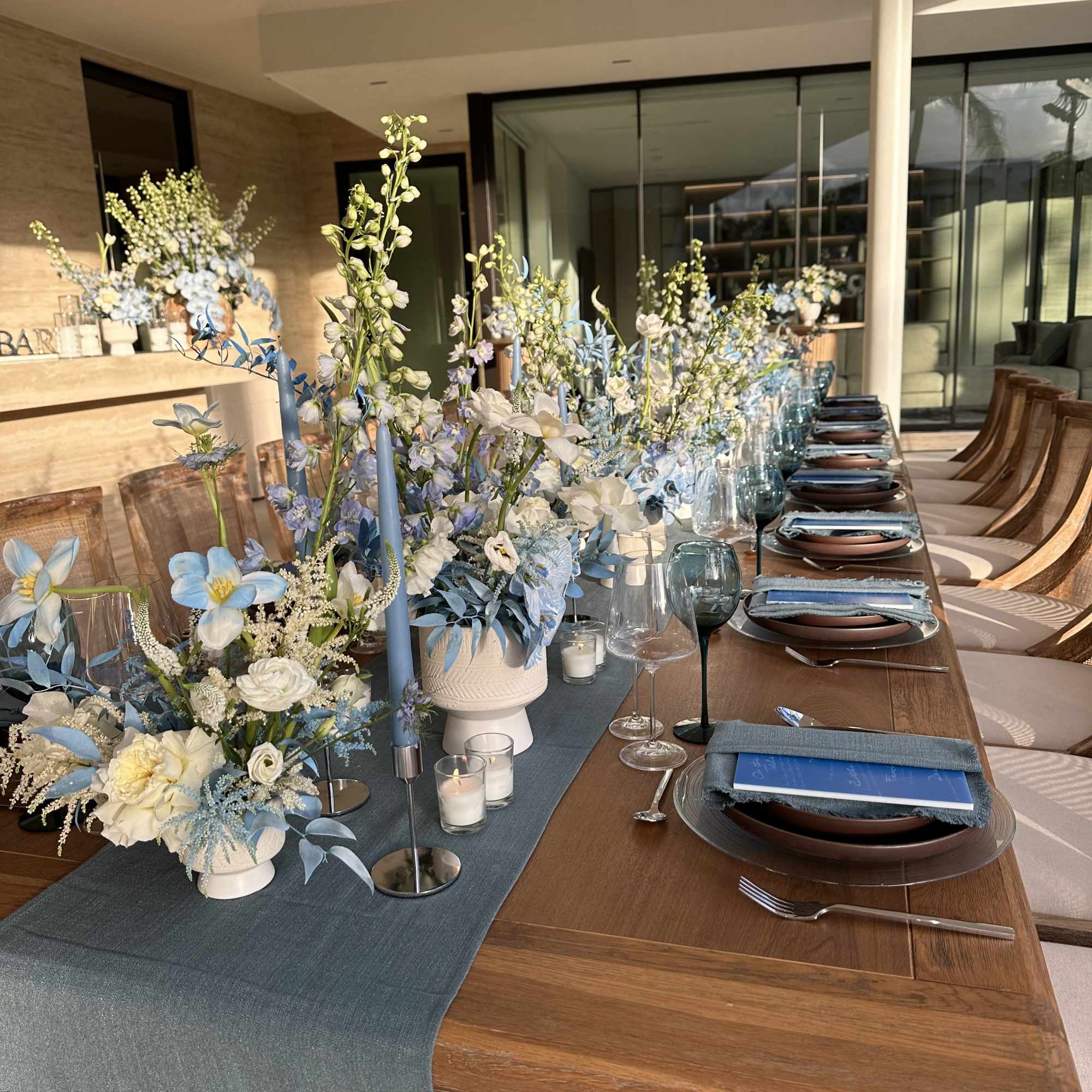 Blue and white floral centerpieces on a long dining table with candles and place settings