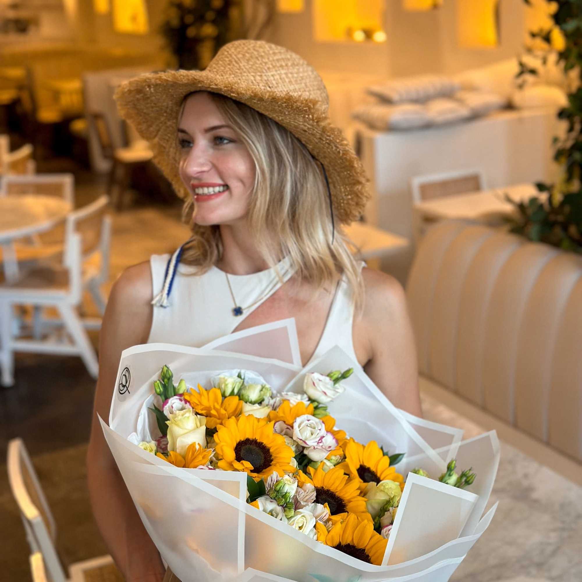 Woman holding a bouquet of sunflowers and white roses in white wrap