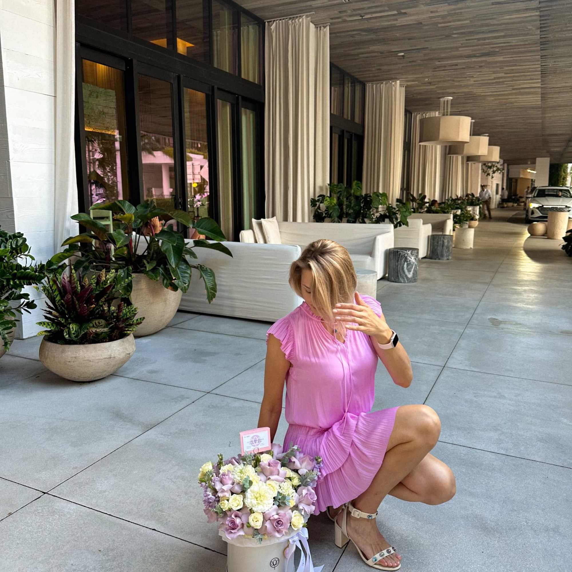 Woman in a pink dress kneels beside a pastel flower box arrangement.