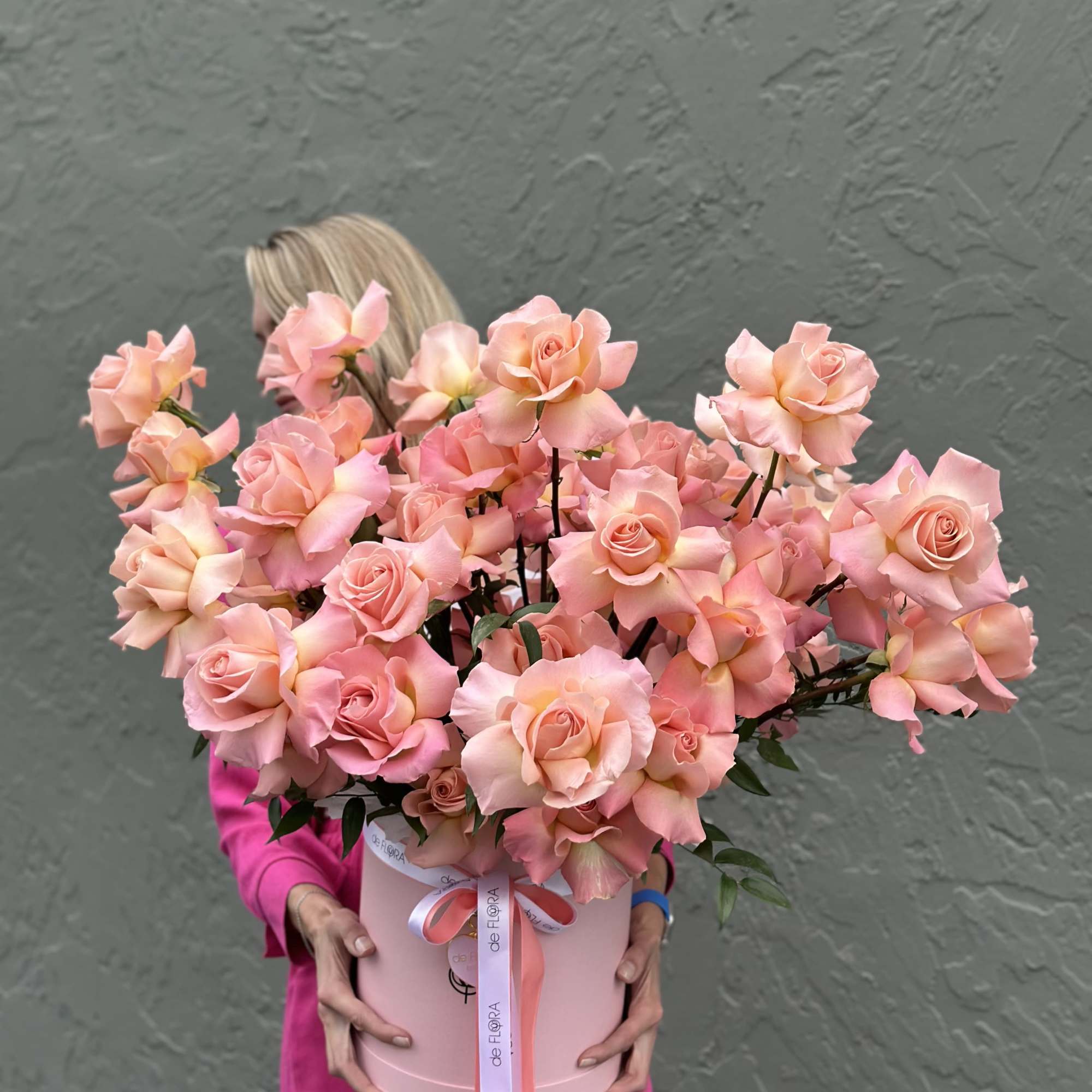 Large pink rose arrangement in a round box held by a woman