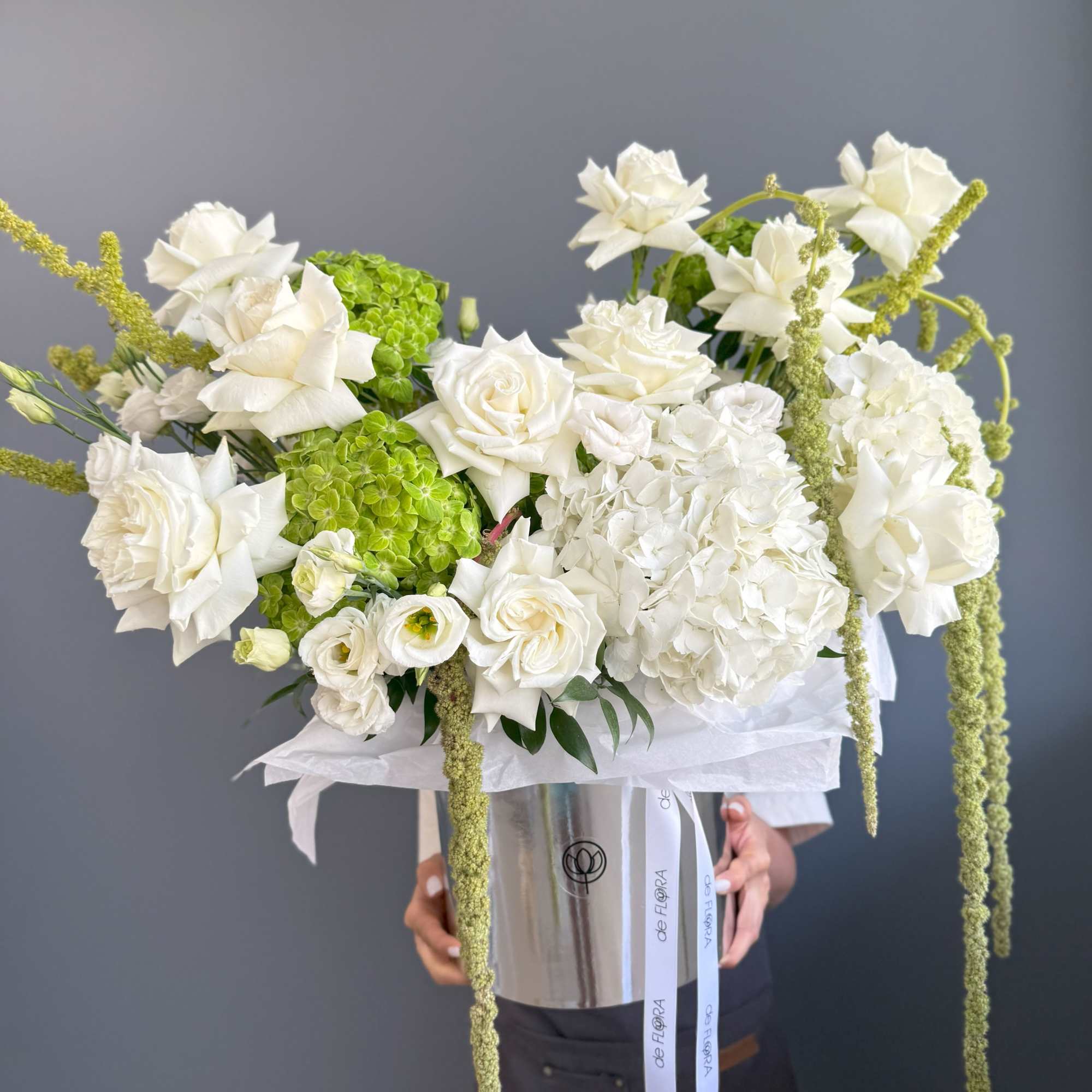 Large white and green rose and hydrangea arrangement in a tall silver vase with trailing green accents