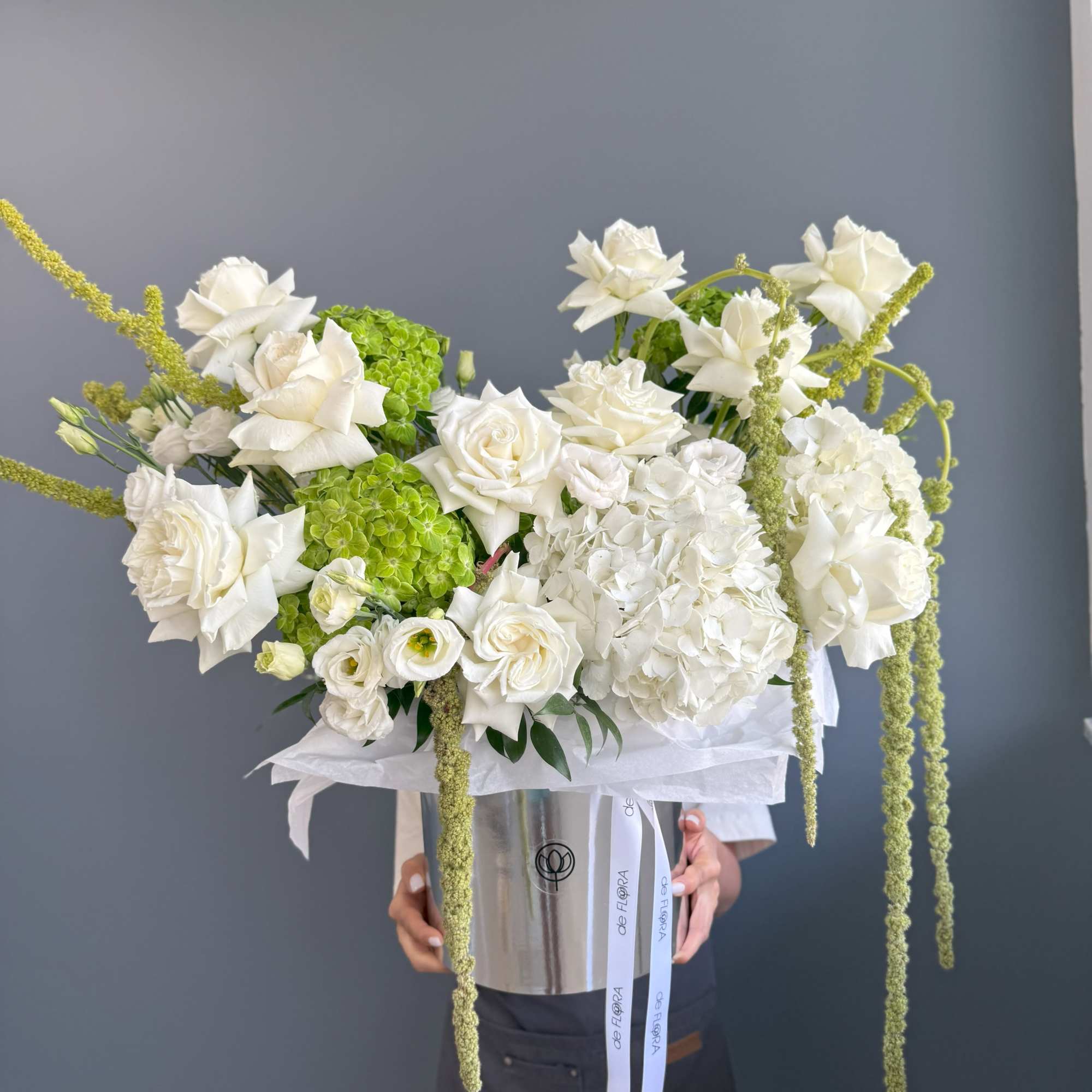 Large white and green arrangement of roses and hydrangeas in a silver hatbox-style container