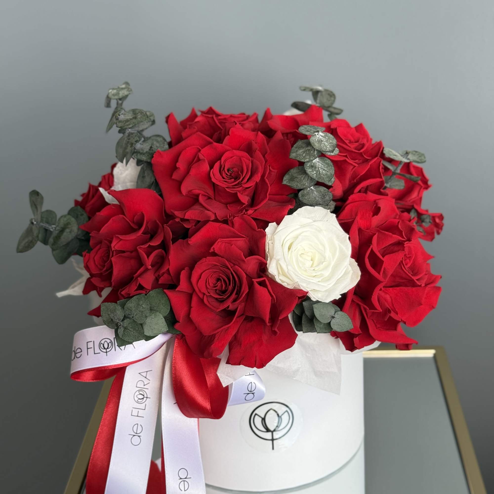 Red and white roses arranged in a white hat box with ribbon
