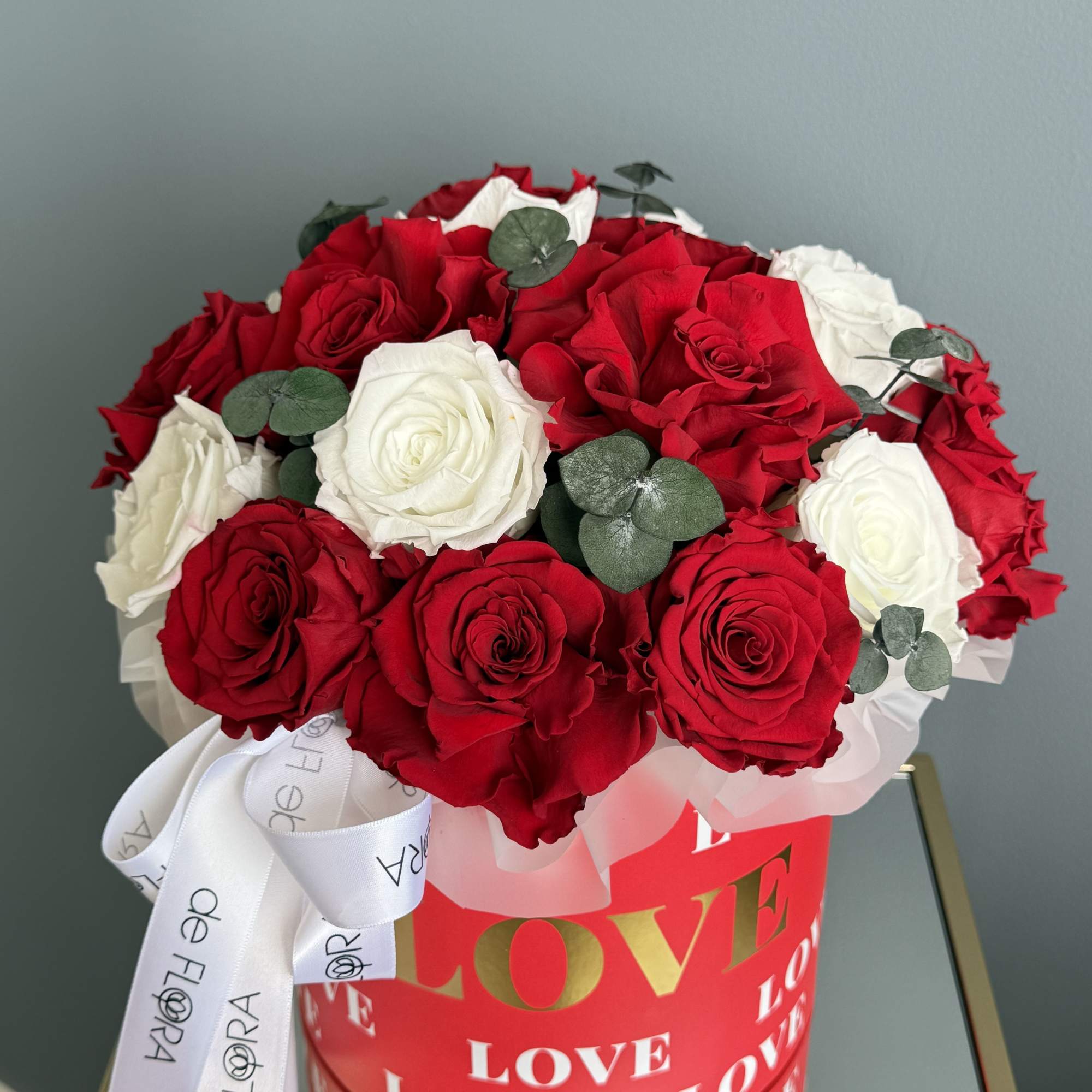 Red and white roses in a red heart-themed box with a white ribbon