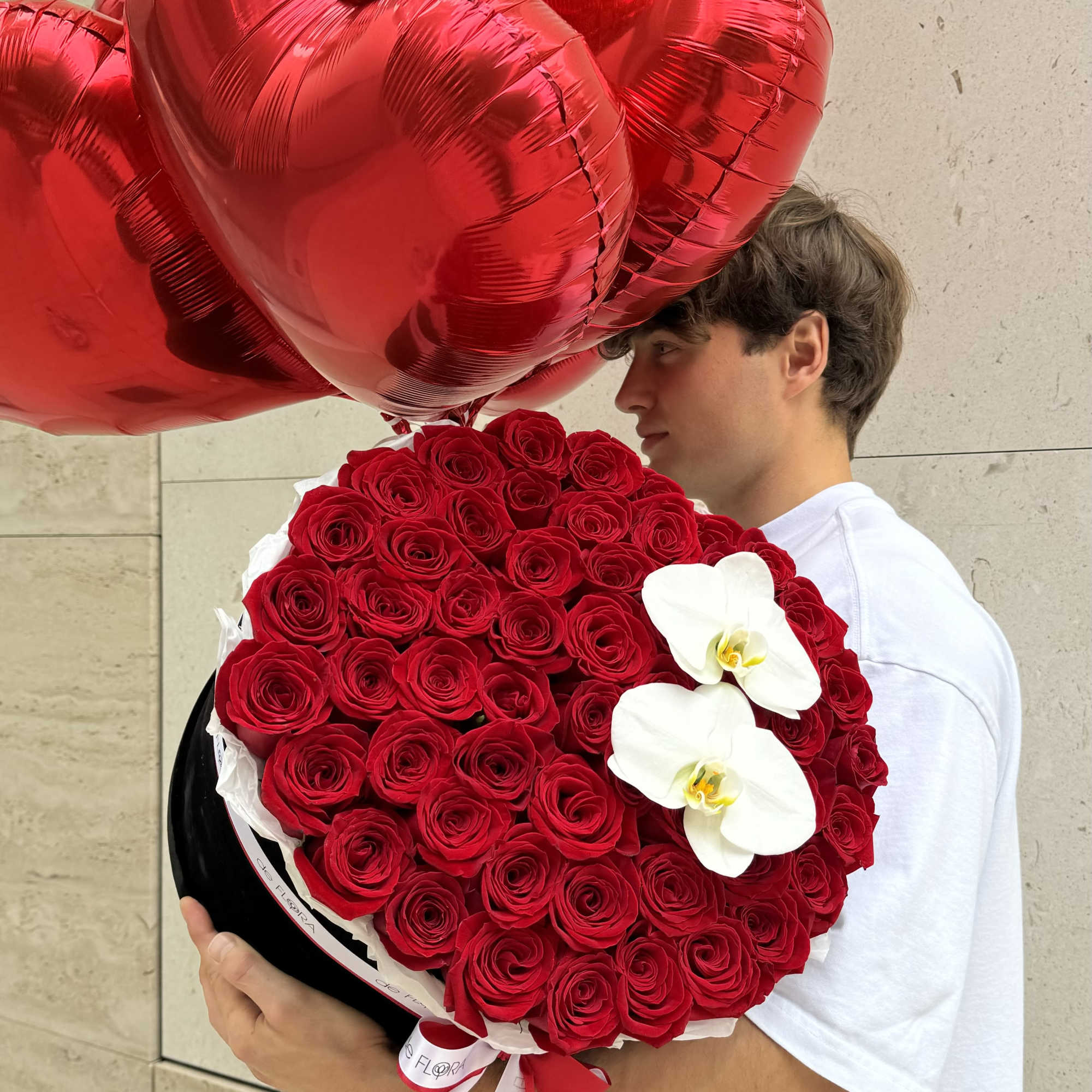 Man holding a bouquet of red roses with white orchids and red heart balloons