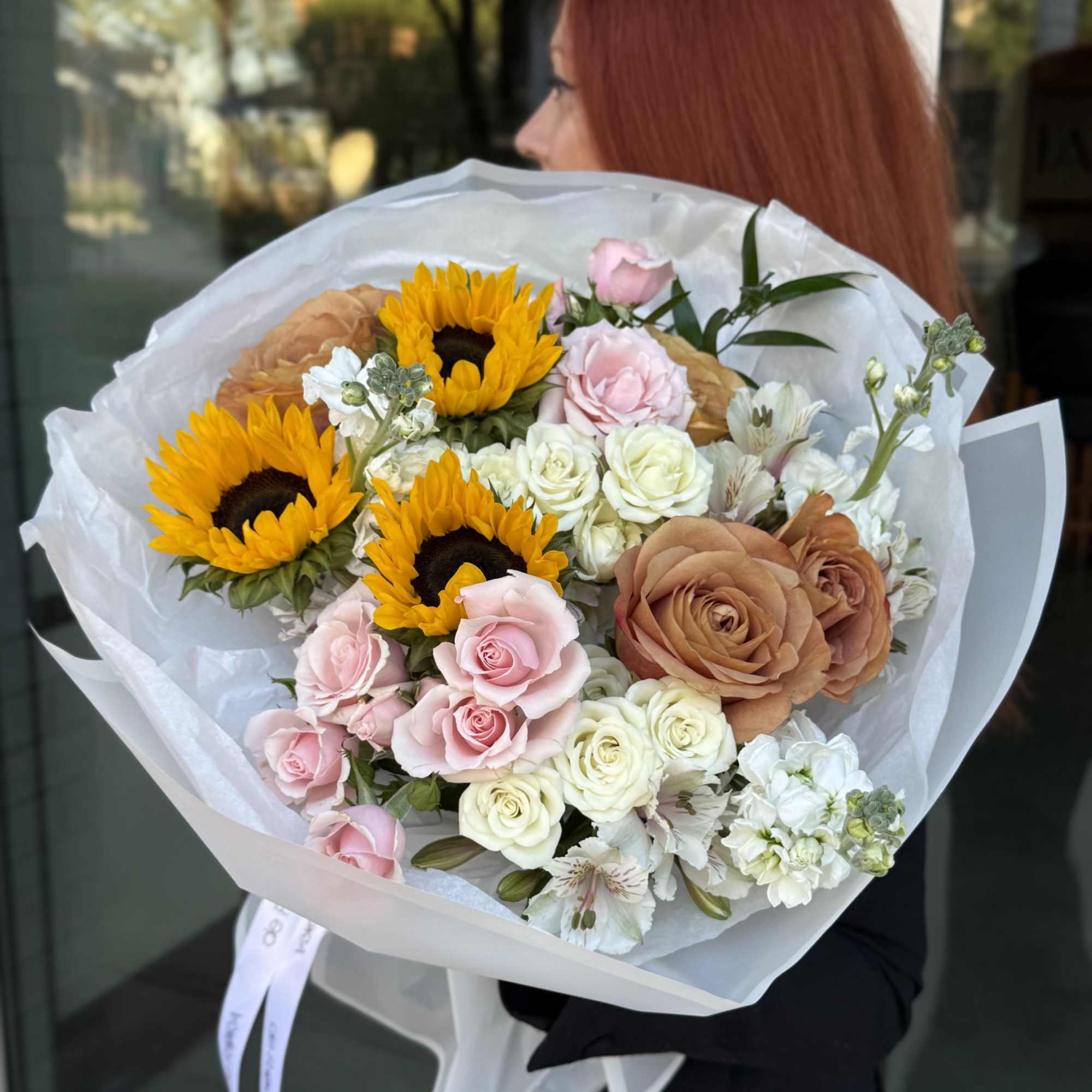 Bouquet of sunflowers, roses, and white blooms wrapped in white paper