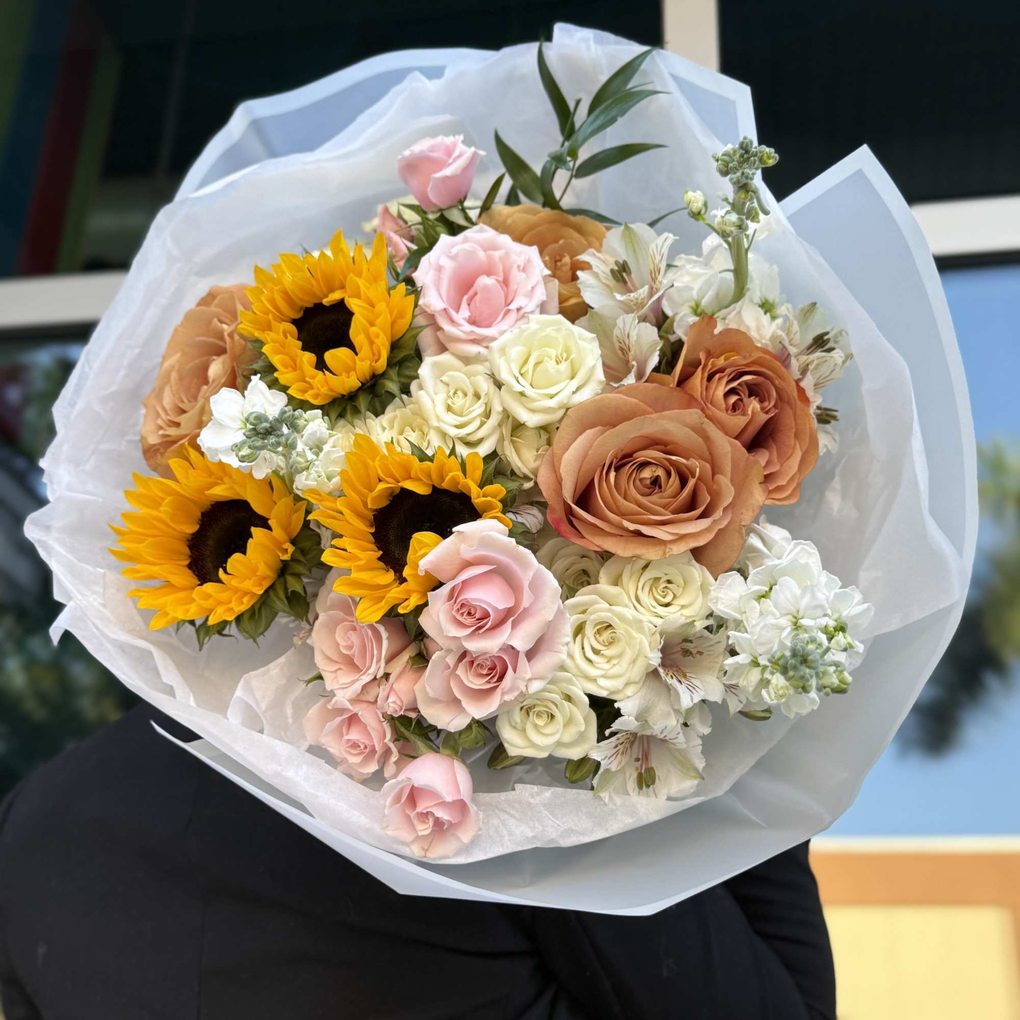 Bouquet of sunflowers, roses, and white blooms wrapped in white paper