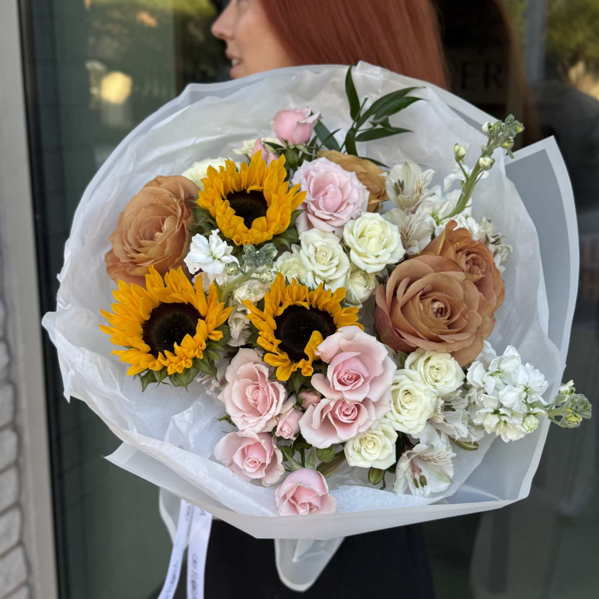Bouquet of sunflowers, roses, and white blooms wrapped in white paper