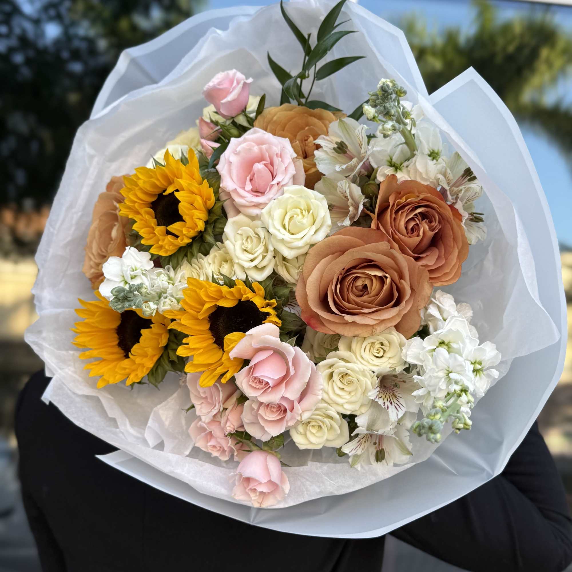 Bouquet of roses, sunflowers, and white blooms wrapped in white paper