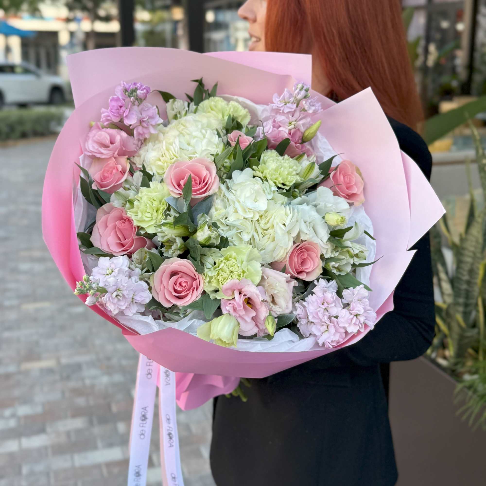 Woman holding a large pink bouquet of roses and pale flowers