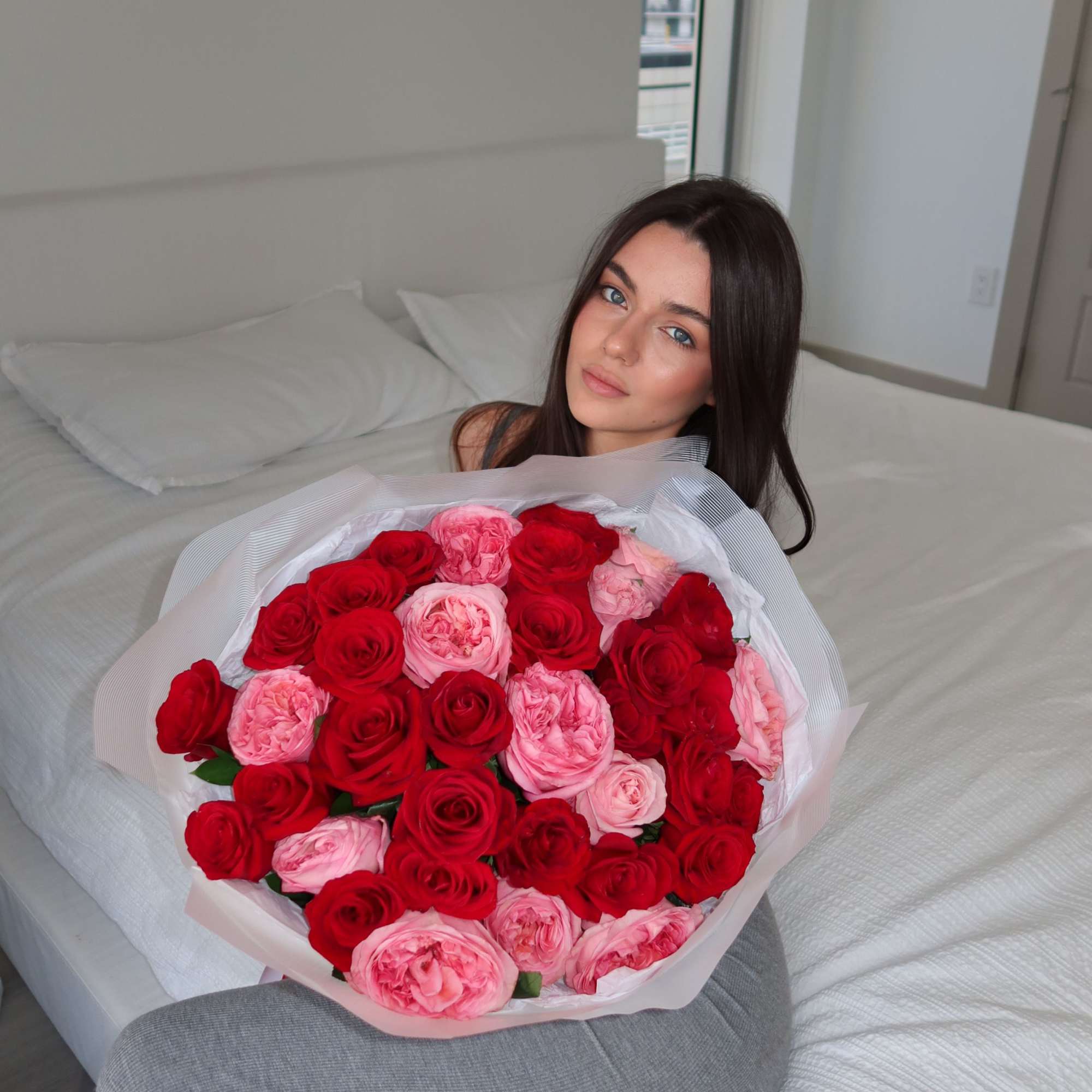 Woman holding a bouquet of red and pink roses on a bed