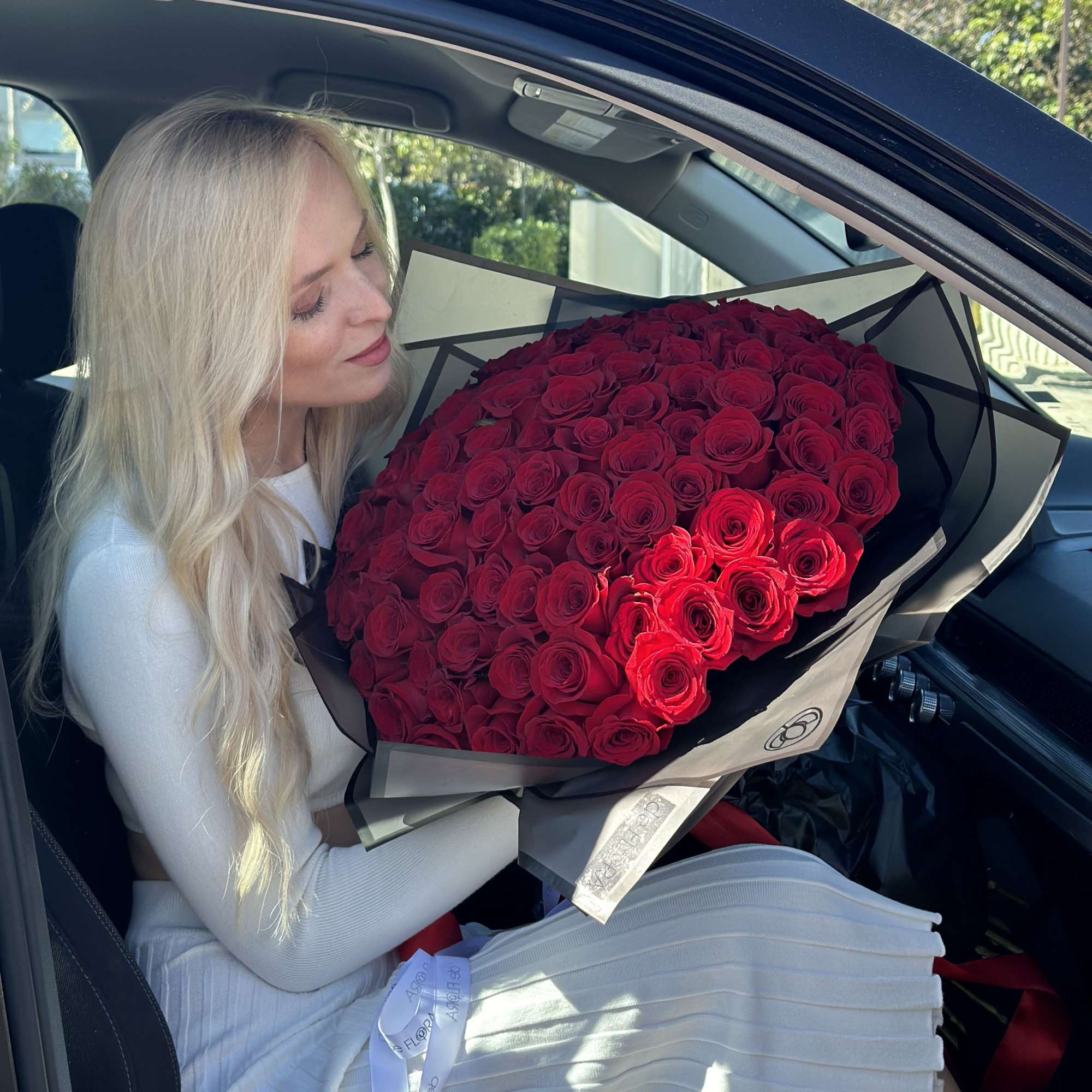Woman holding a large bouquet of red roses in a car
