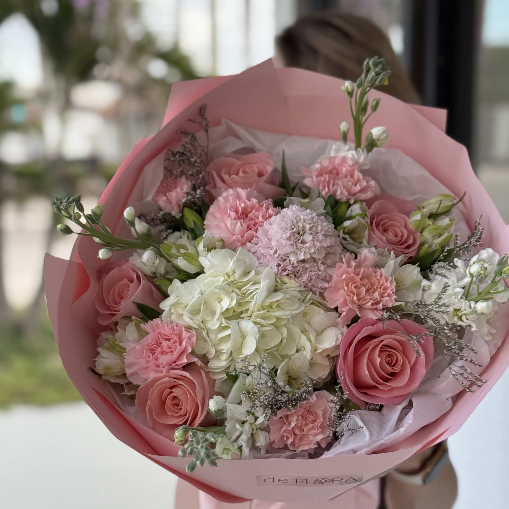 Pink and white bouquet of roses, carnations, and hydrangea wrapped in pink paper