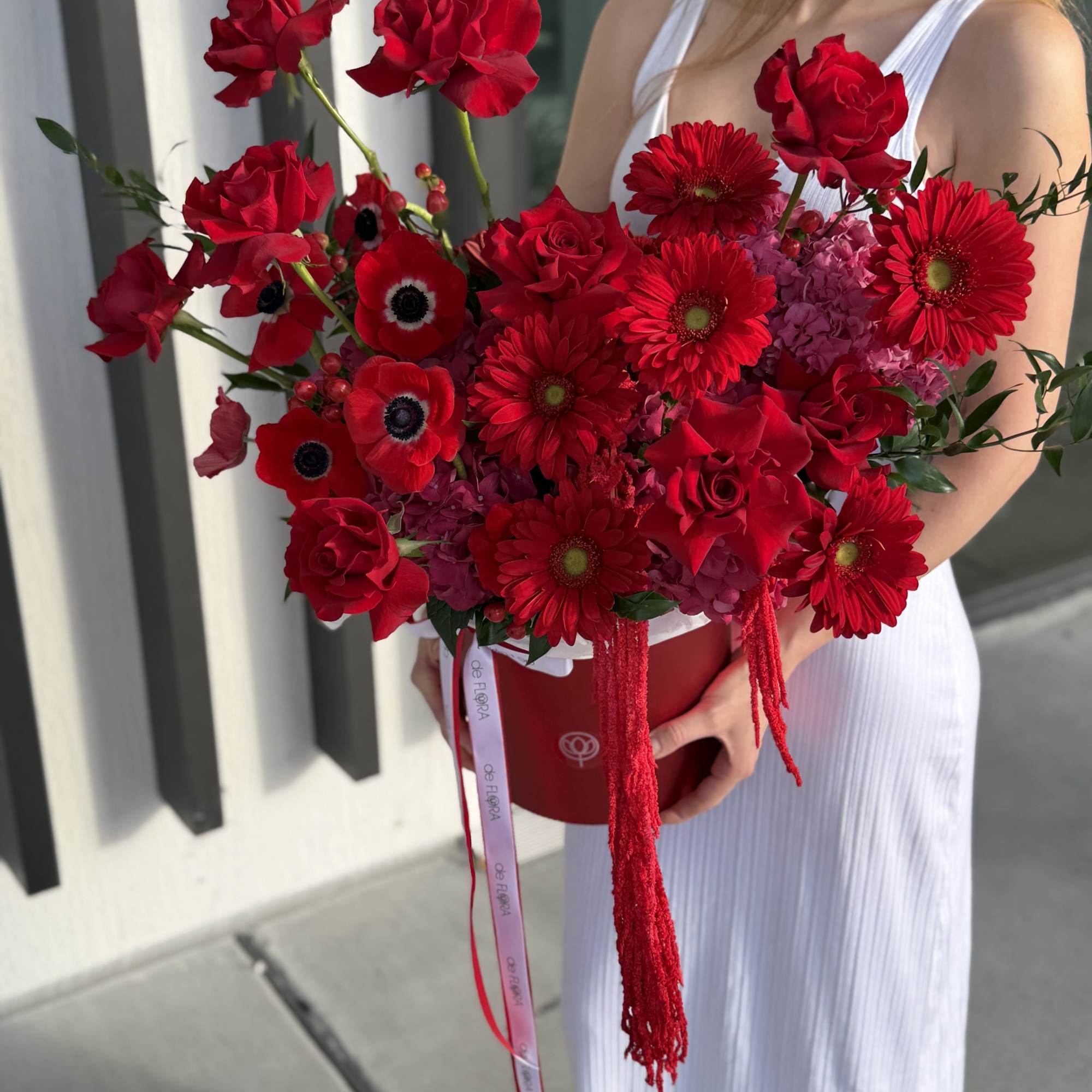 Woman holding a large bouquet of red roses and gerbera daisies in a red box