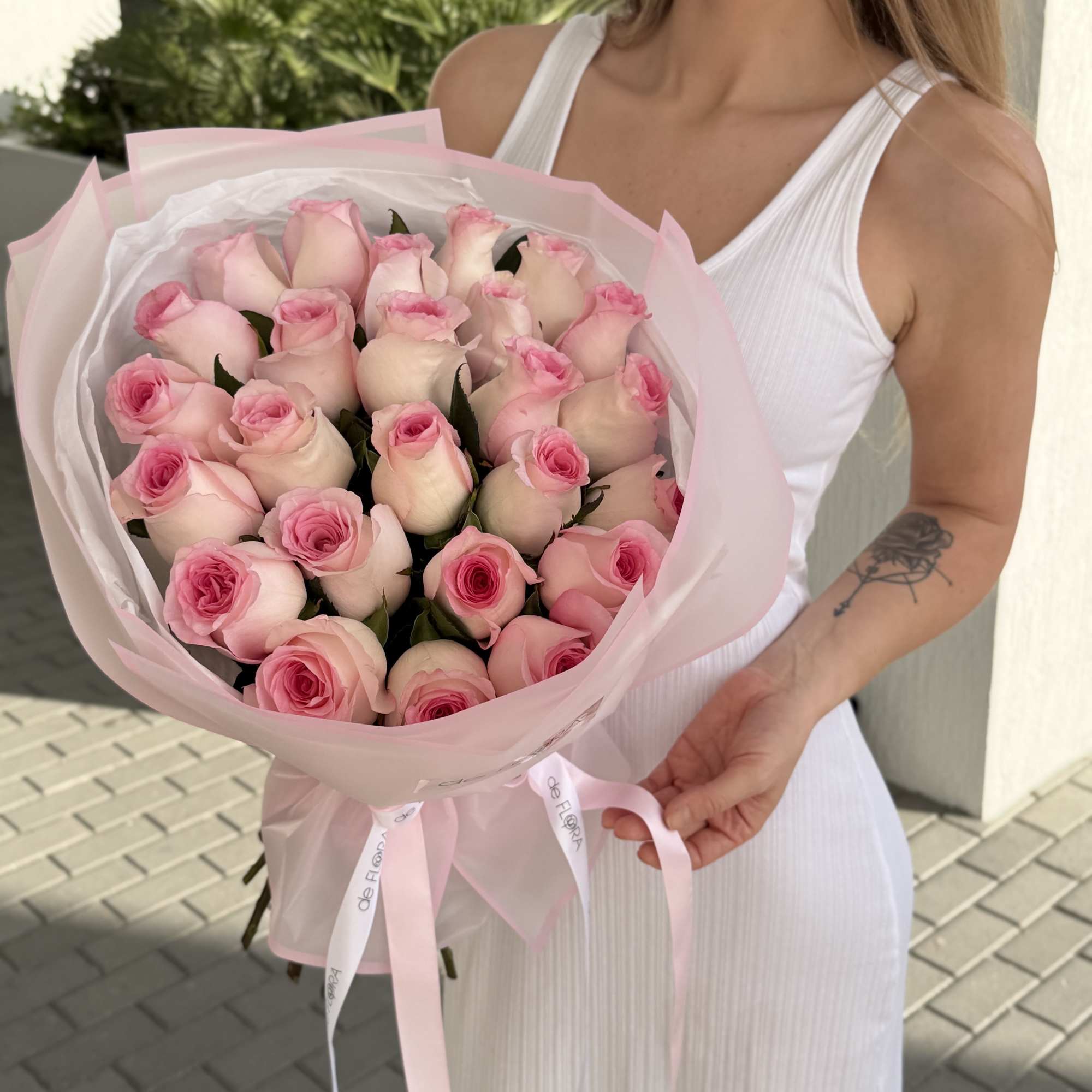 Woman holding a large bouquet of pale pink roses wrapped in pink paper