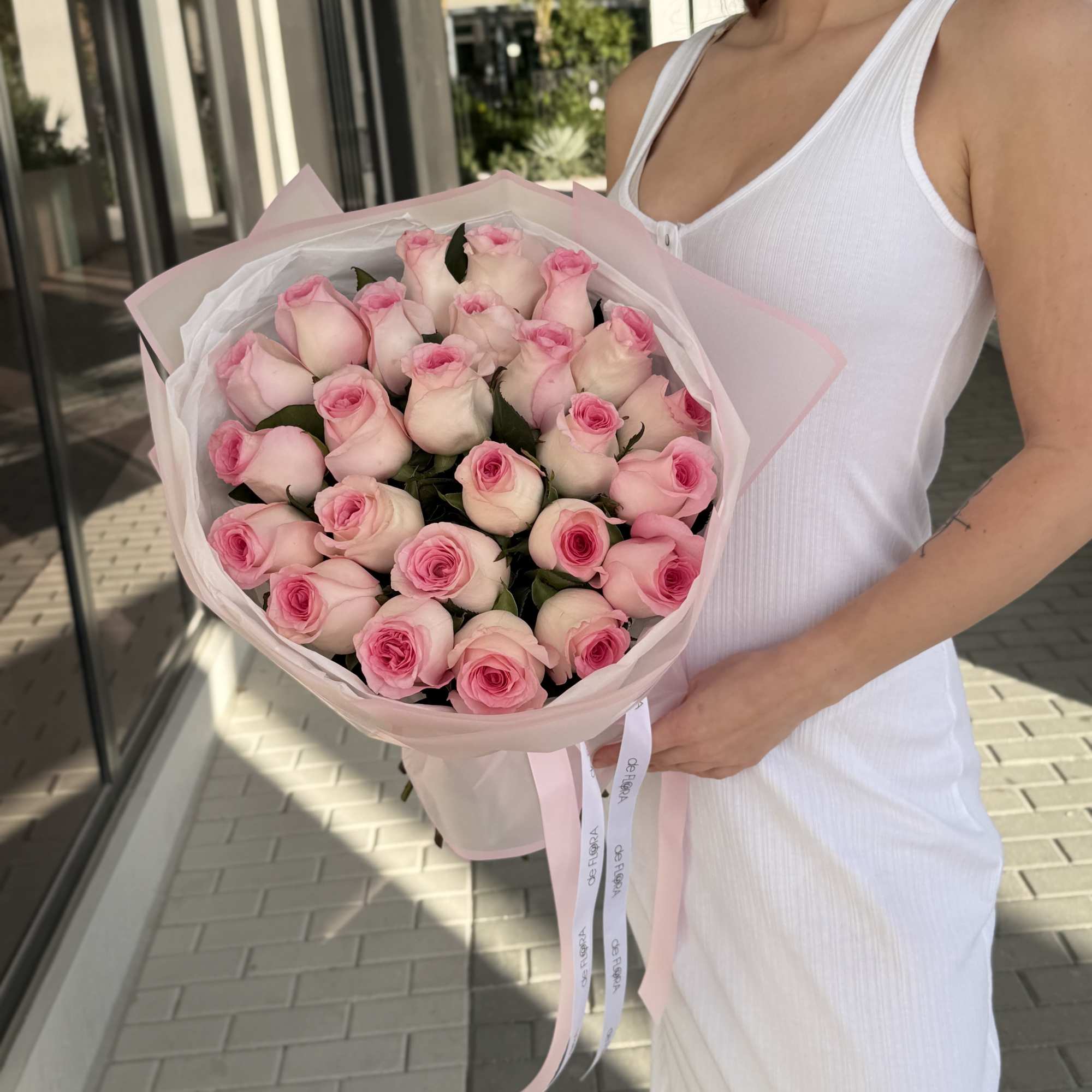 Woman holding a bouquet of pale pink roses wrapped in pink paper