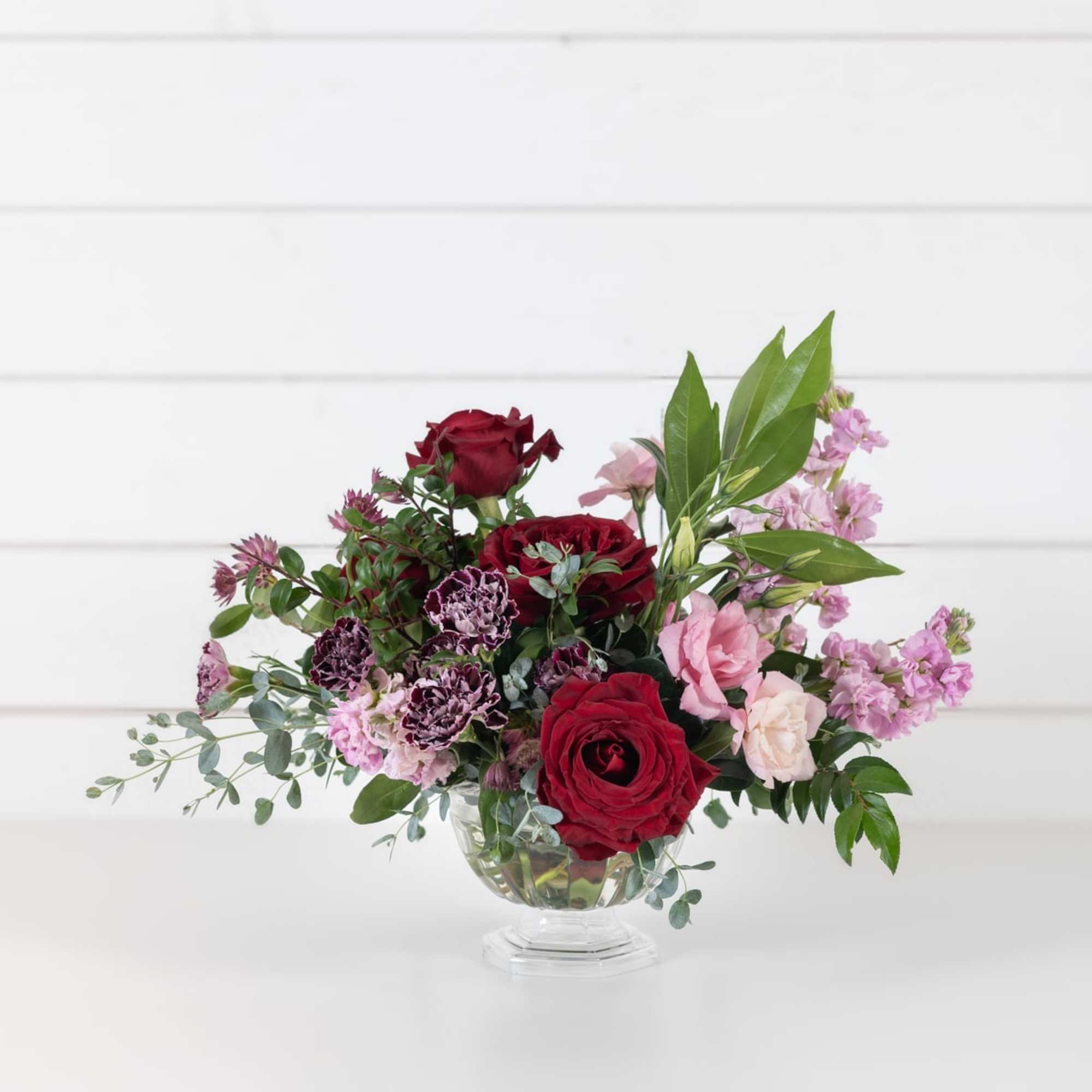 Red and pink roses with purple carnations in a clear glass vase