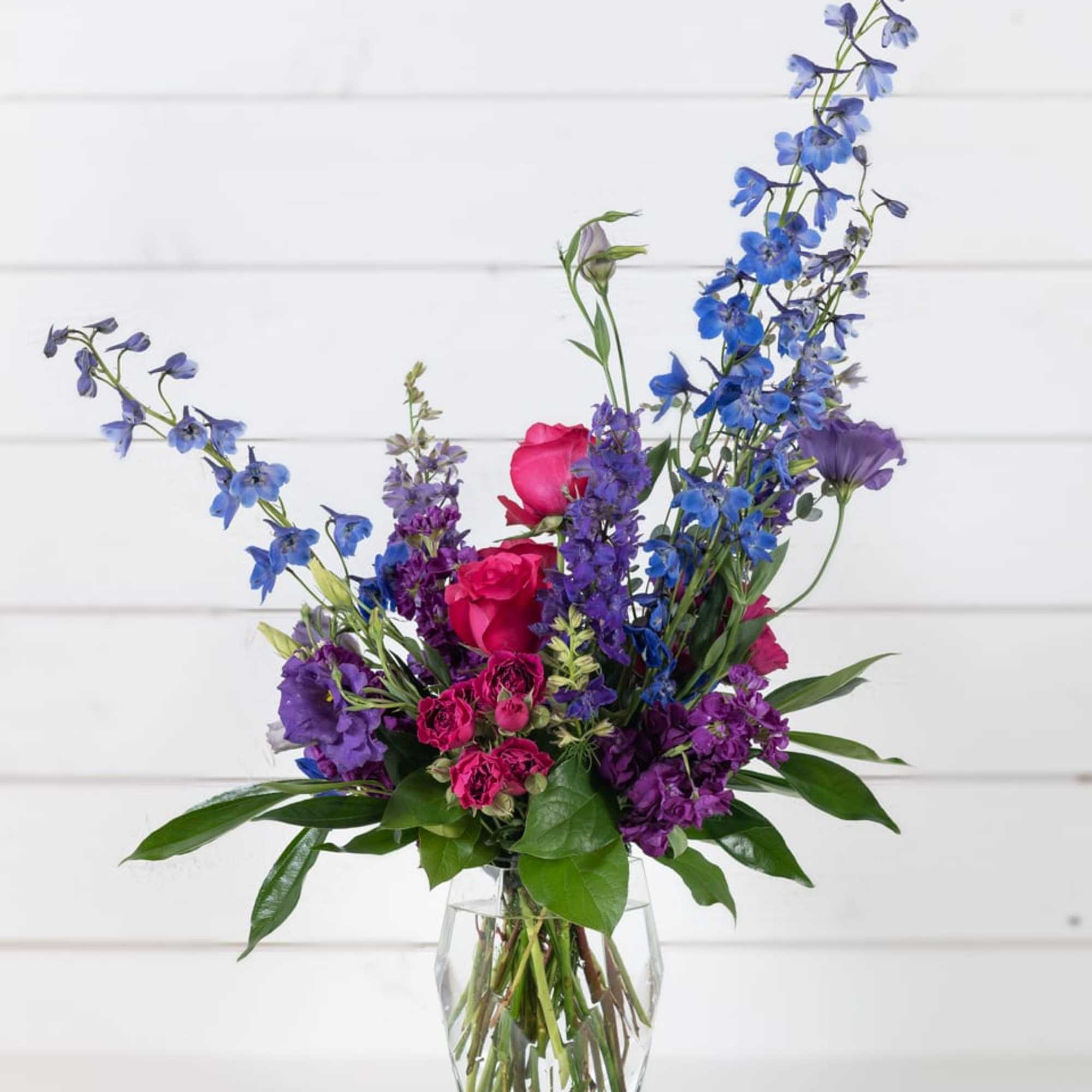 Blue and purple mixed bouquet with pink roses in a clear glass vase