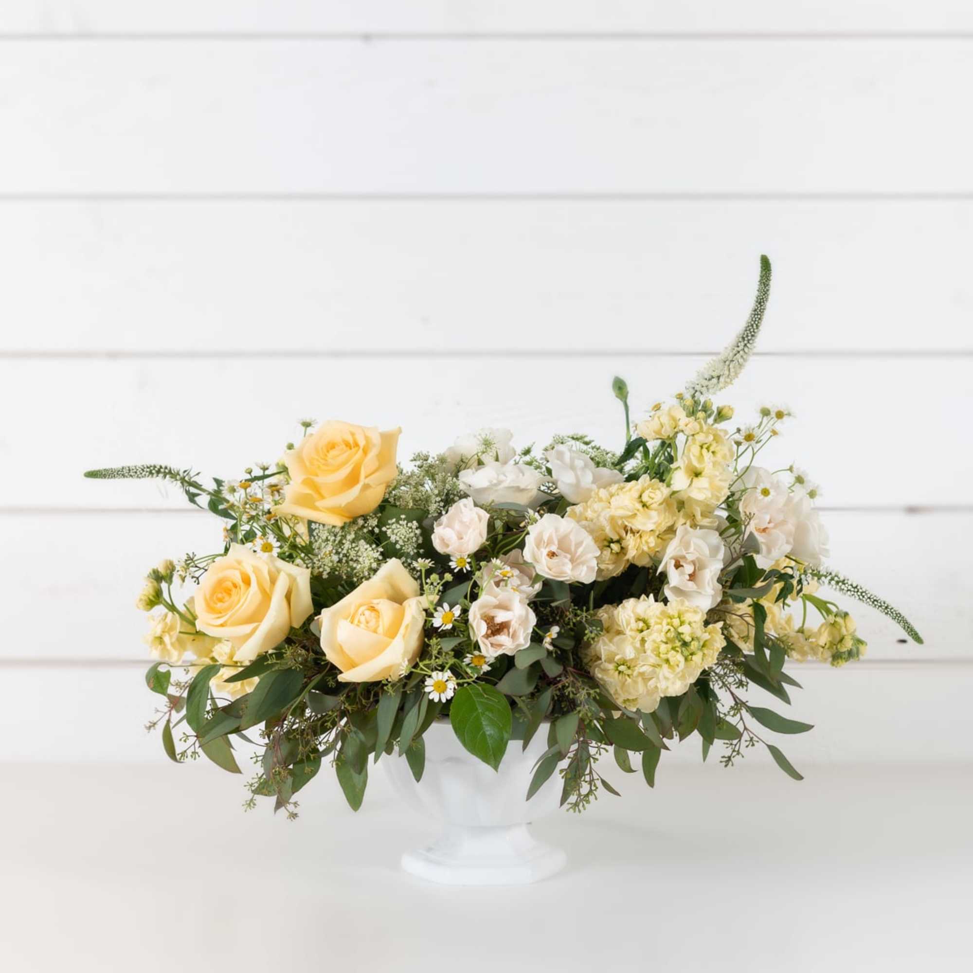 Cream and yellow flower arrangement in a white pedestal vase