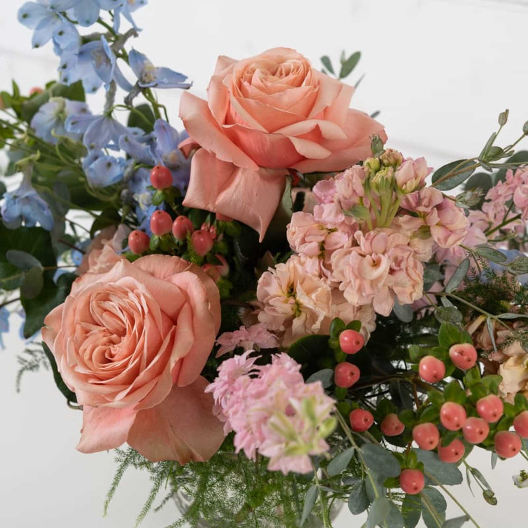 Peach roses and blue flowers in a clear glass vase