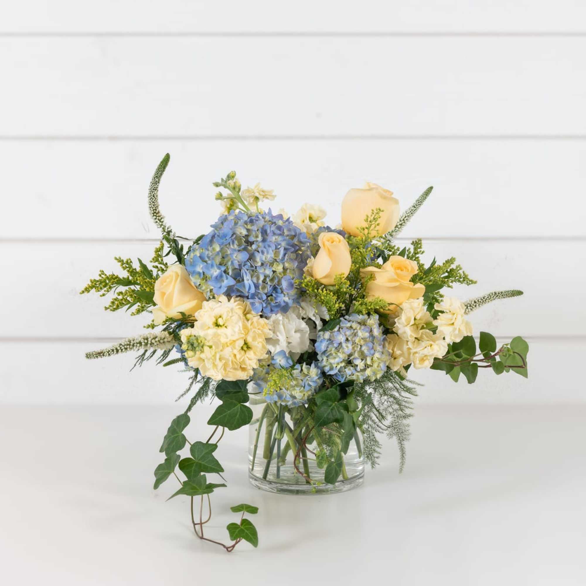 Blue hydrangeas and pale yellow roses in a clear glass vase