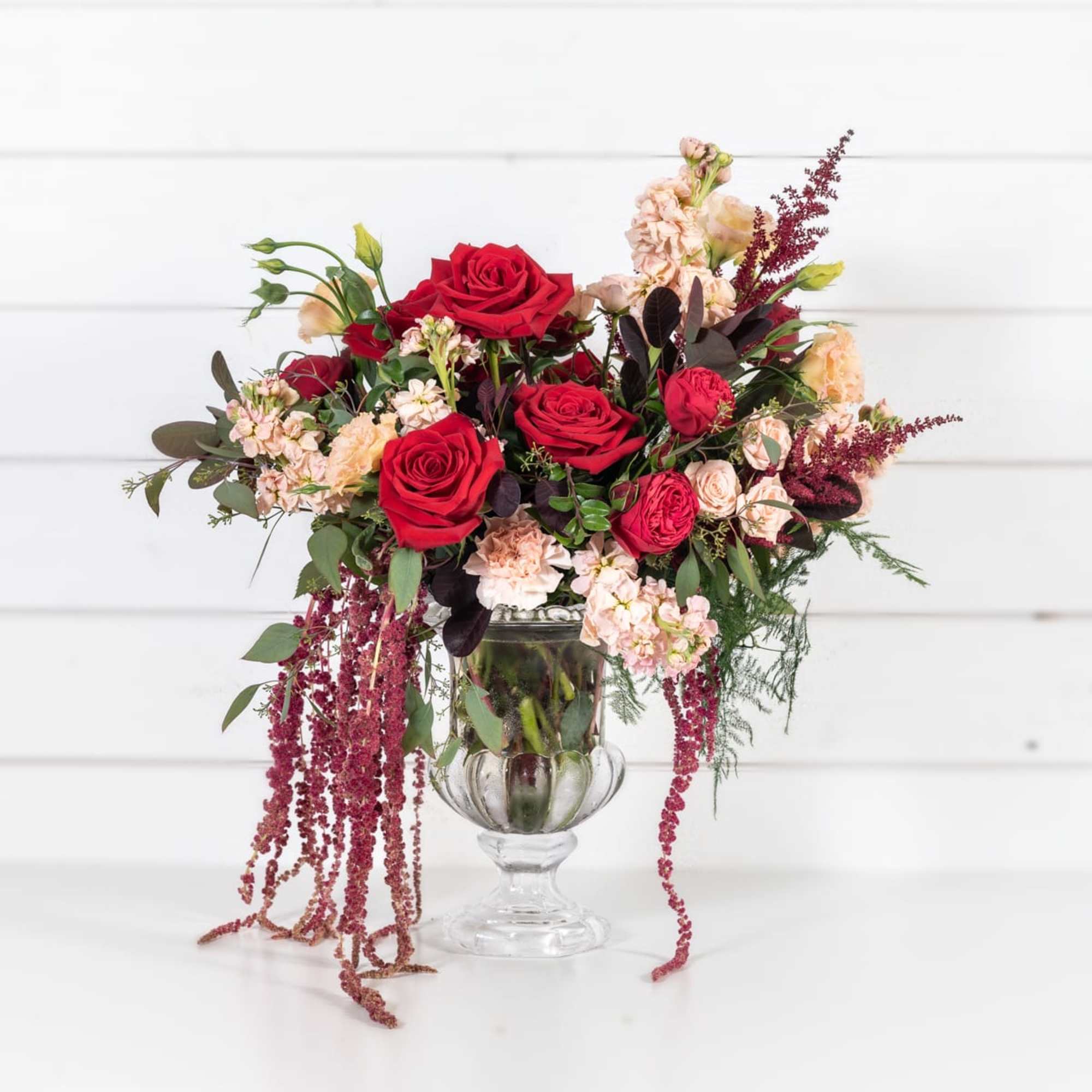 Red roses and blush flowers in a clear glass vase