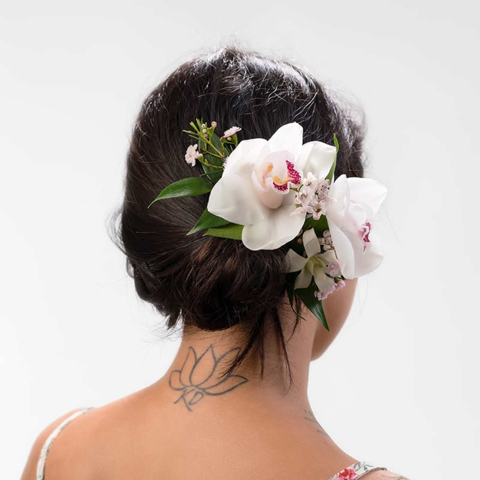 White orchids and small pink flowers worn as a hairpiece in an updo