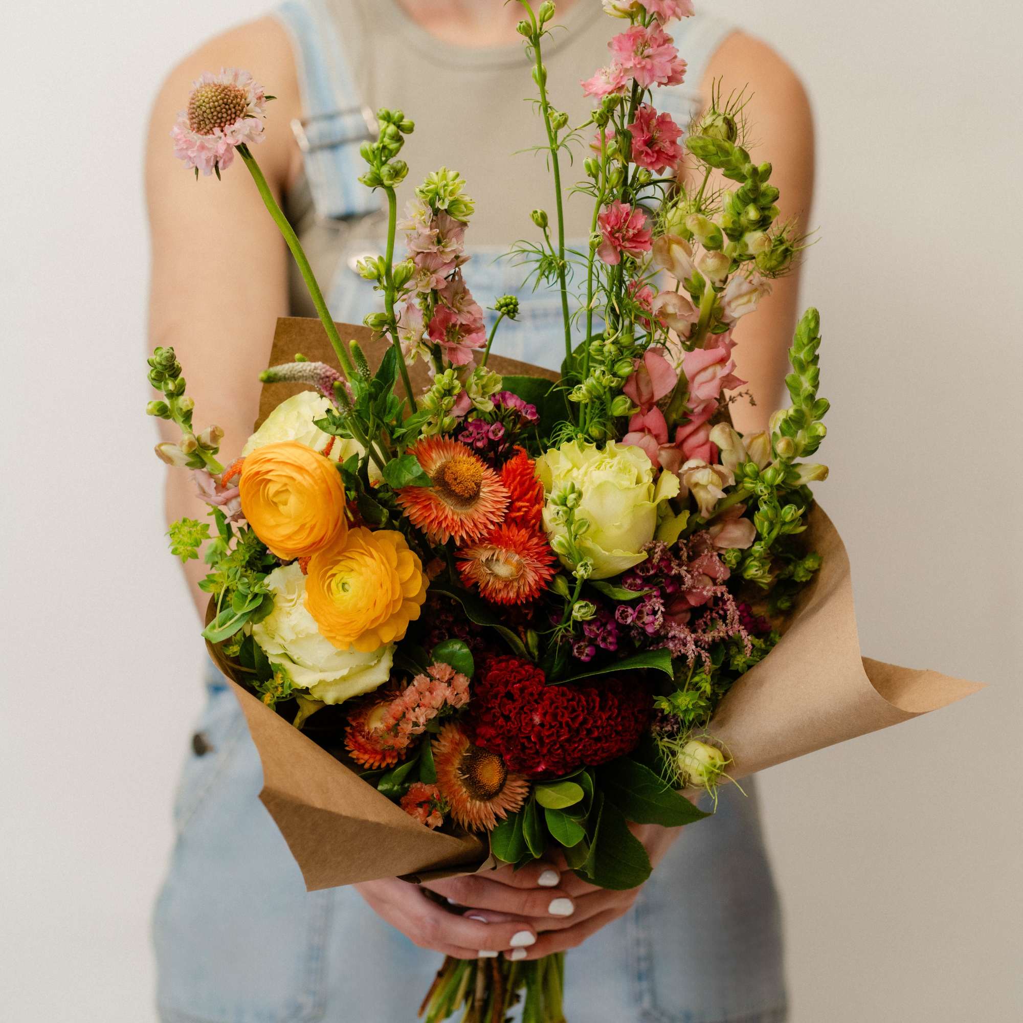 Mixed bouquet of orange, pink, and cream flowers wrapped in brown paper