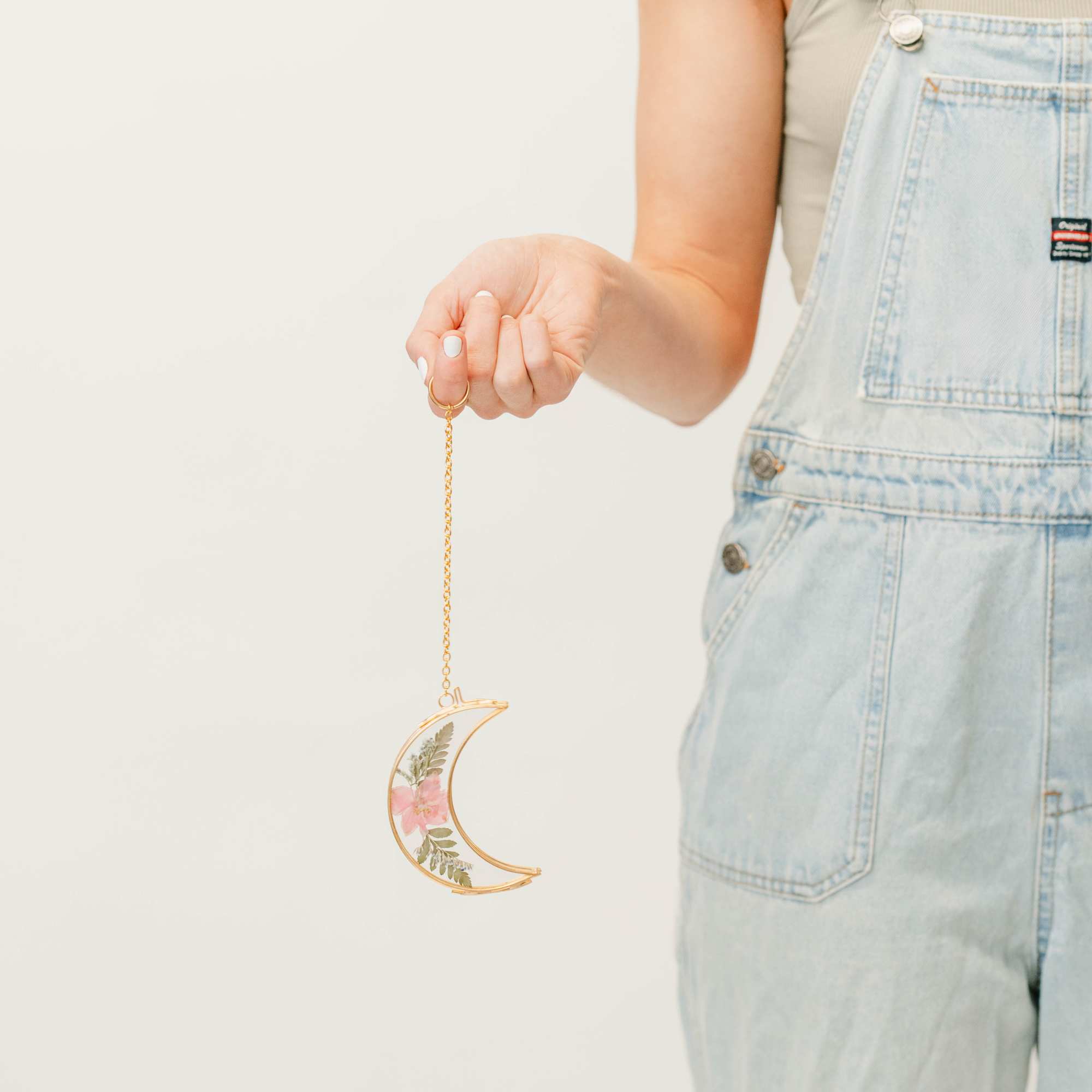 Person holding a crescent-shaped floral ornament on a gold chain