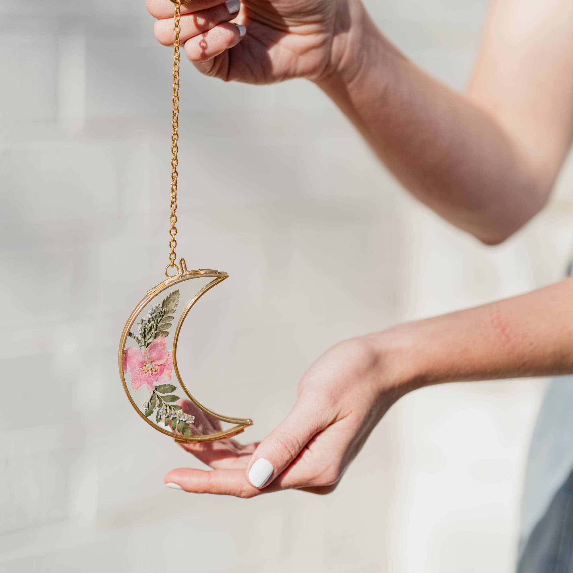 Hands holding a gold crescent ornament with pressed pink flowers