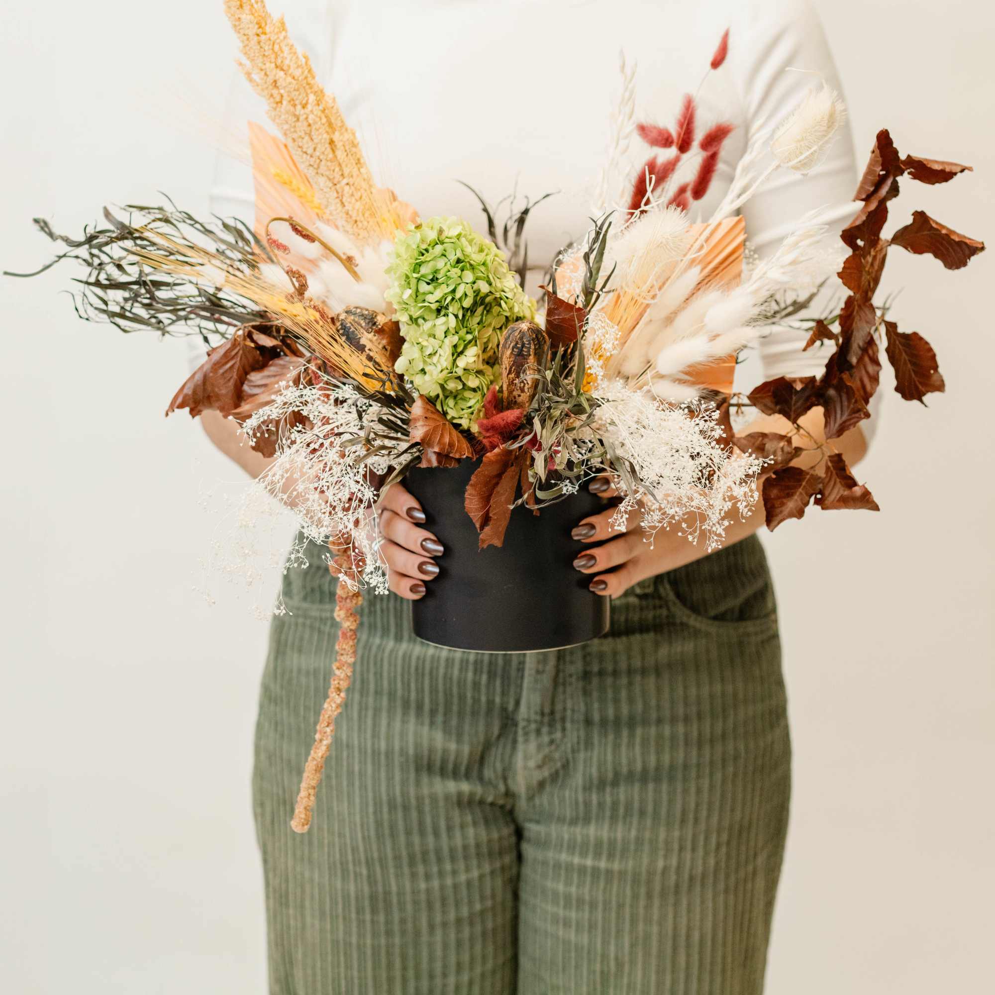 Person holding a dried floral arrangement in a black vase