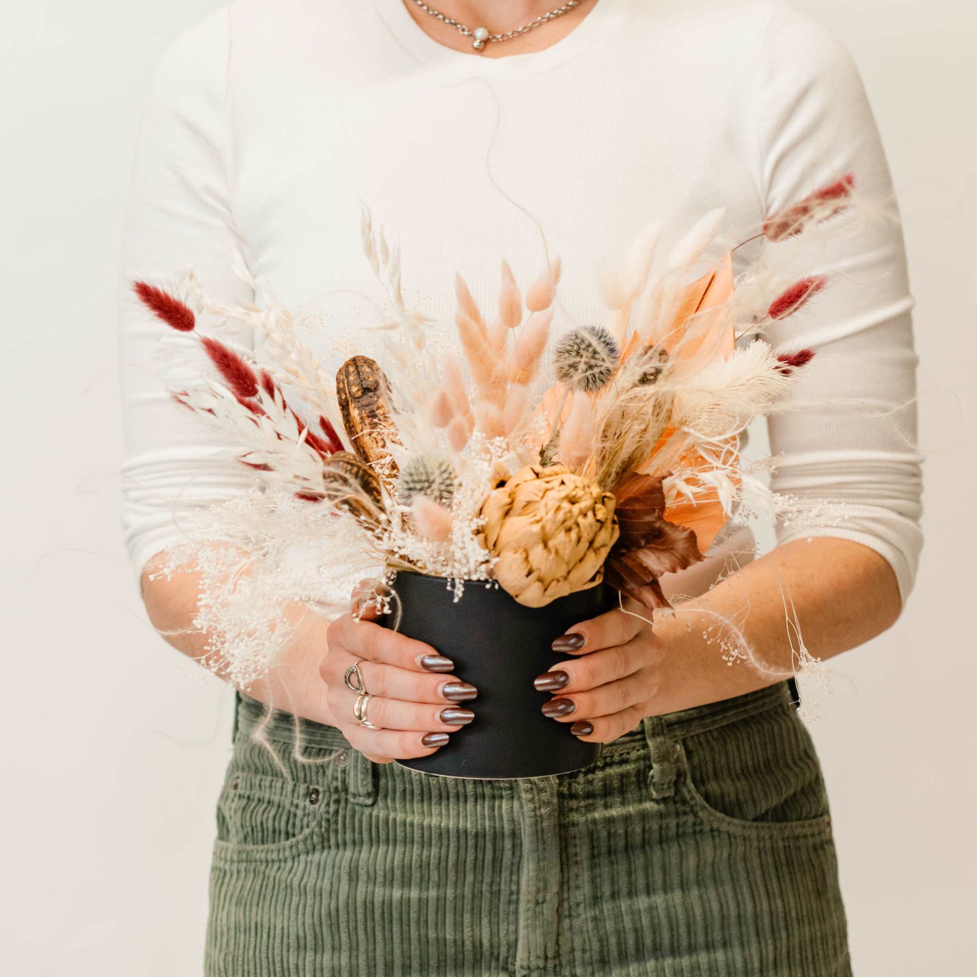 Woman holding a dried floral arrangement in a black vase