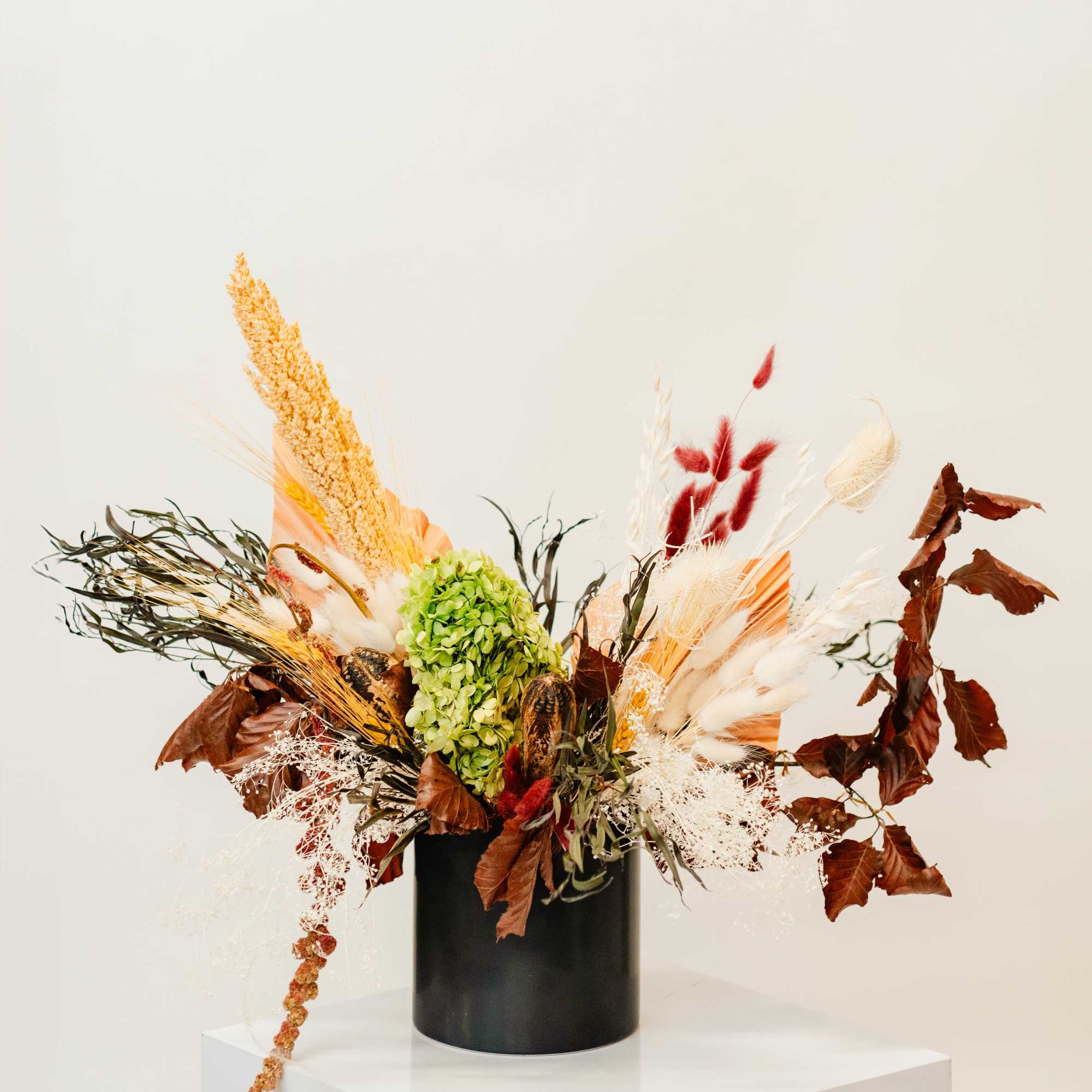 Dried floral arrangement in a black vase with green hydrangea and tan, white, and red accents