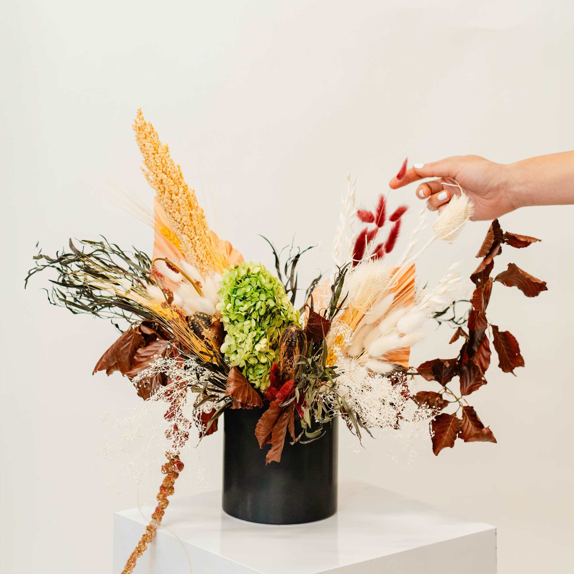 Dried floral arrangement in a black vase with green hydrangea and feathery grasses