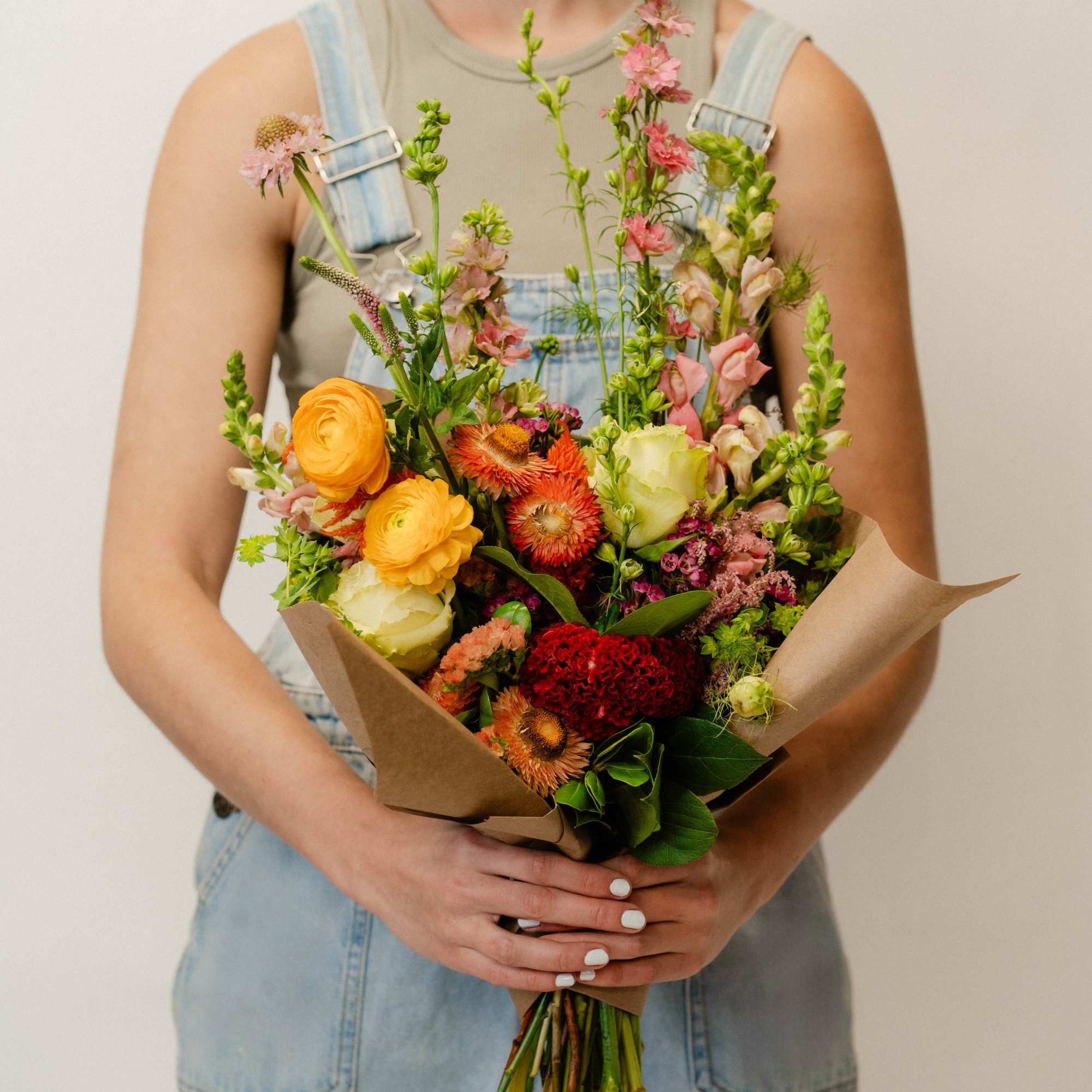Person holding a colorful mixed bouquet wrapped in brown paper
