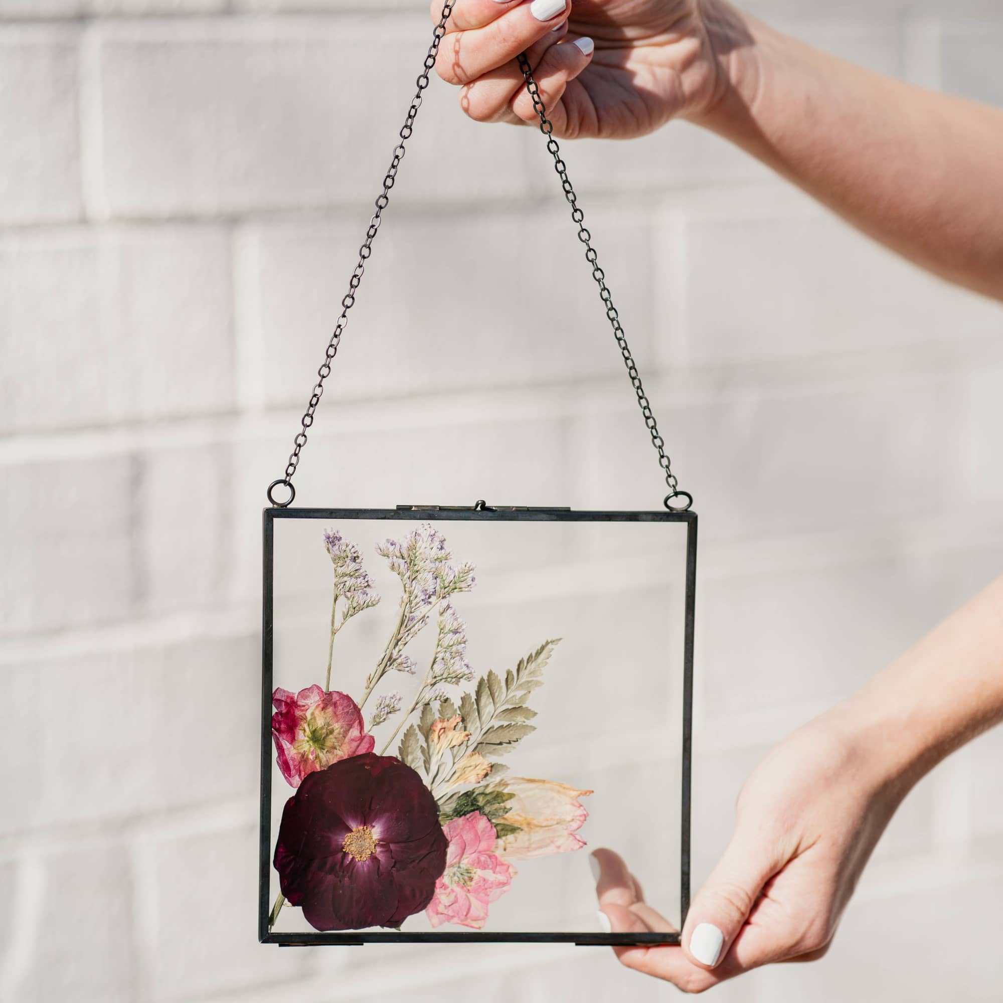 Pressed flowers in a hanging glass frame with a black chain