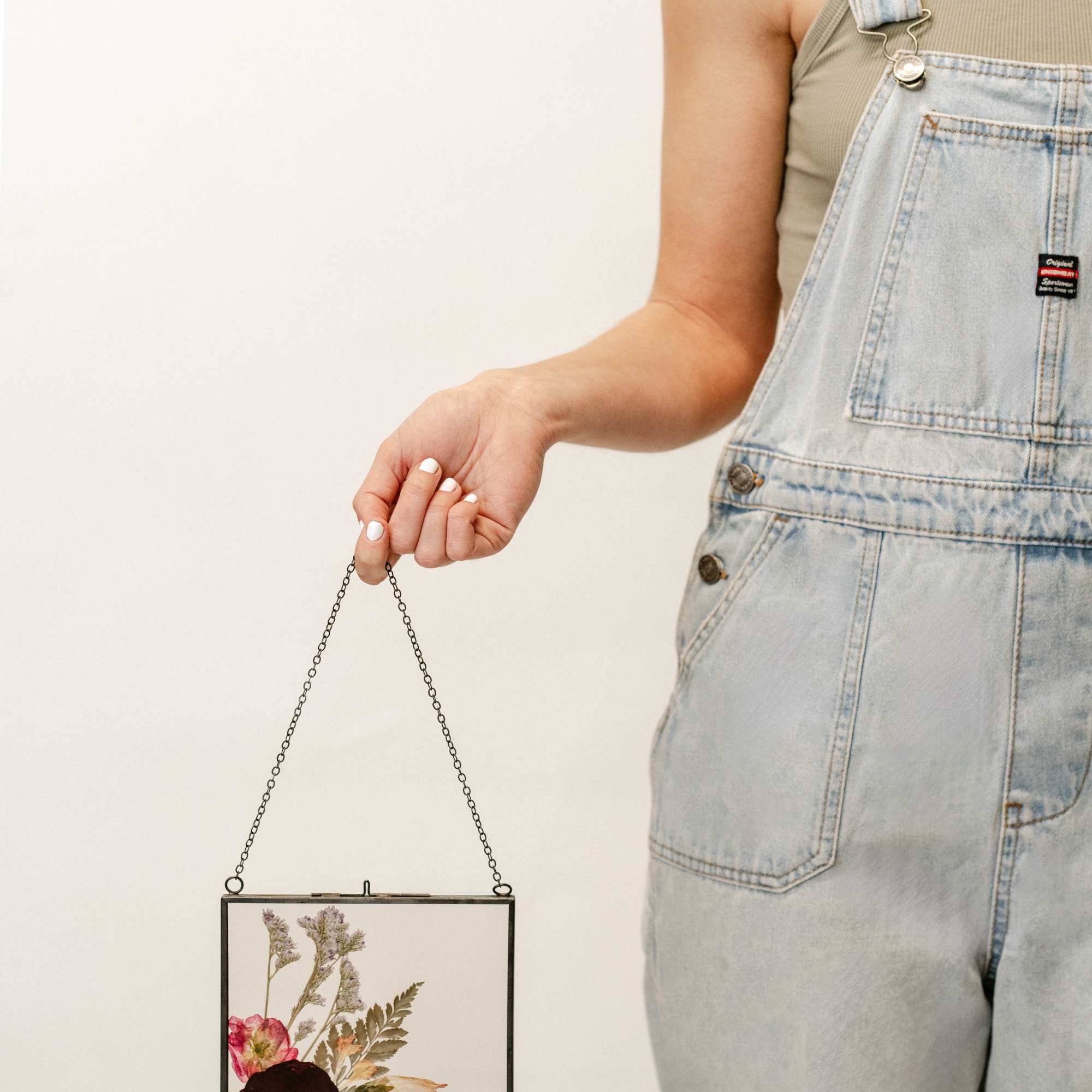 Person holding a hanging glass frame with pressed flowers