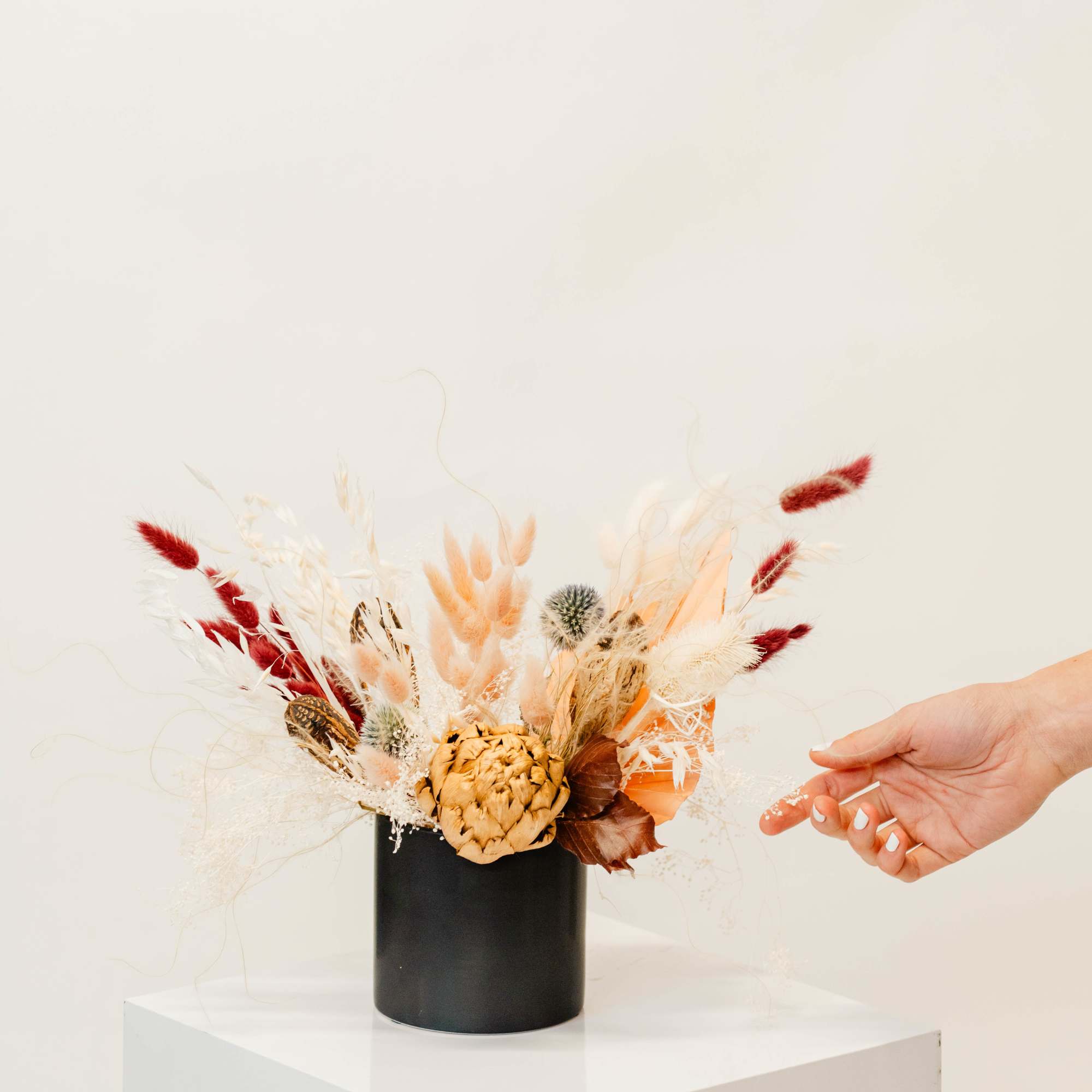 Dried floral arrangement in a black vase with red and cream accents