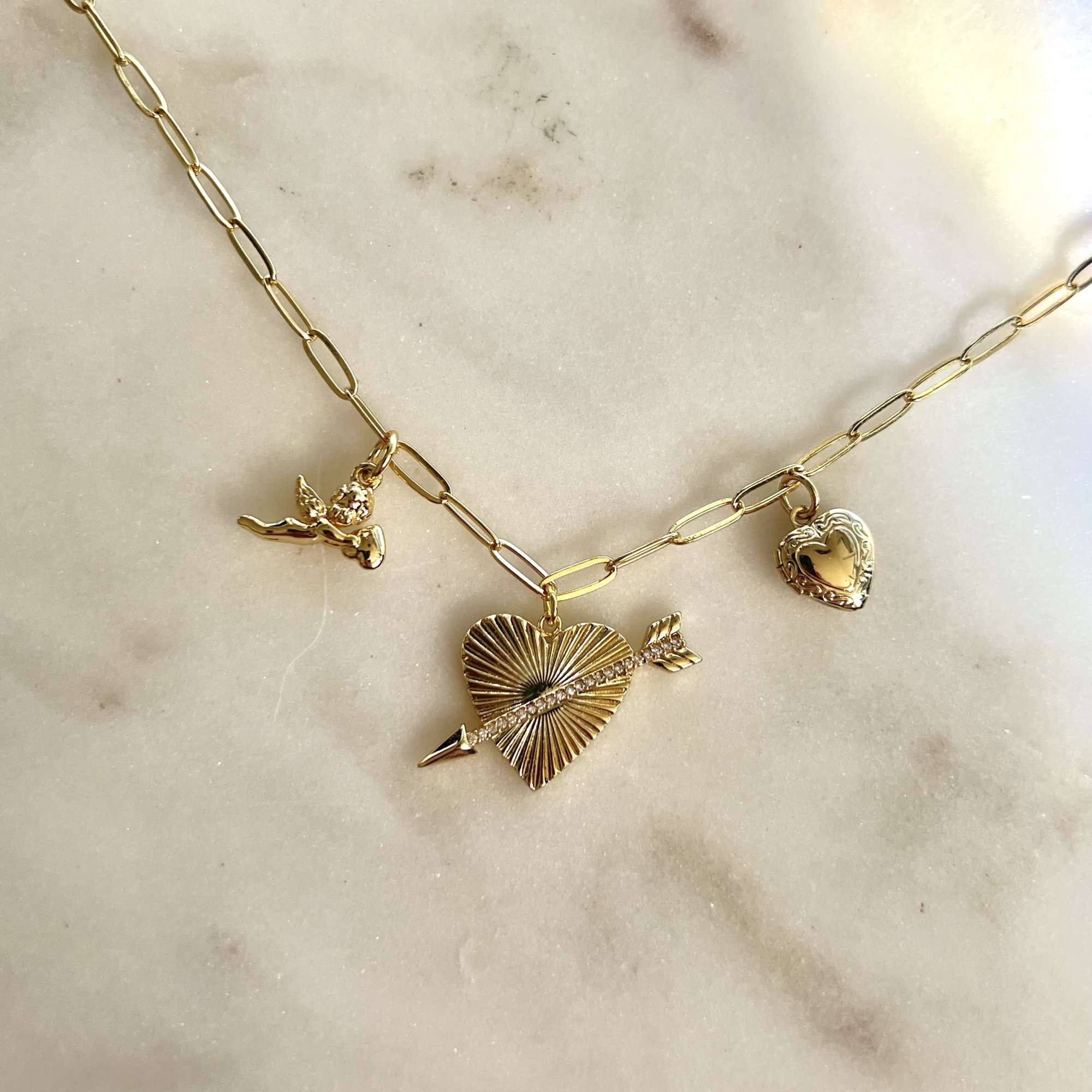 Gold charm necklace with heart and angel pendants on a marble surface