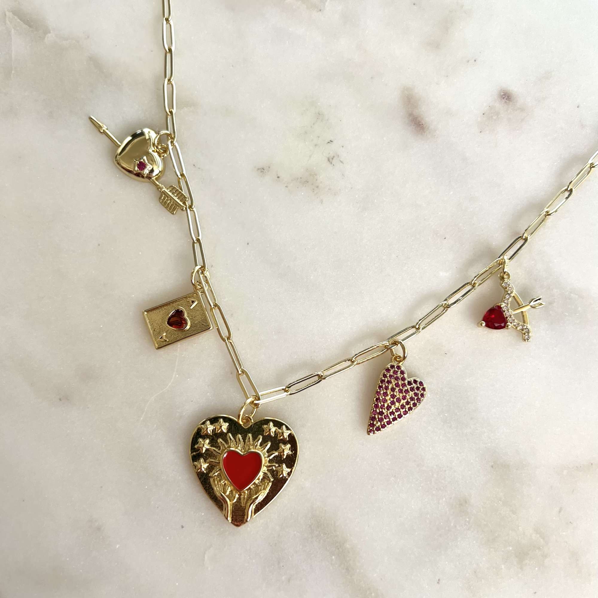 Gold charm necklace with heart-shaped pendants on a marble surface