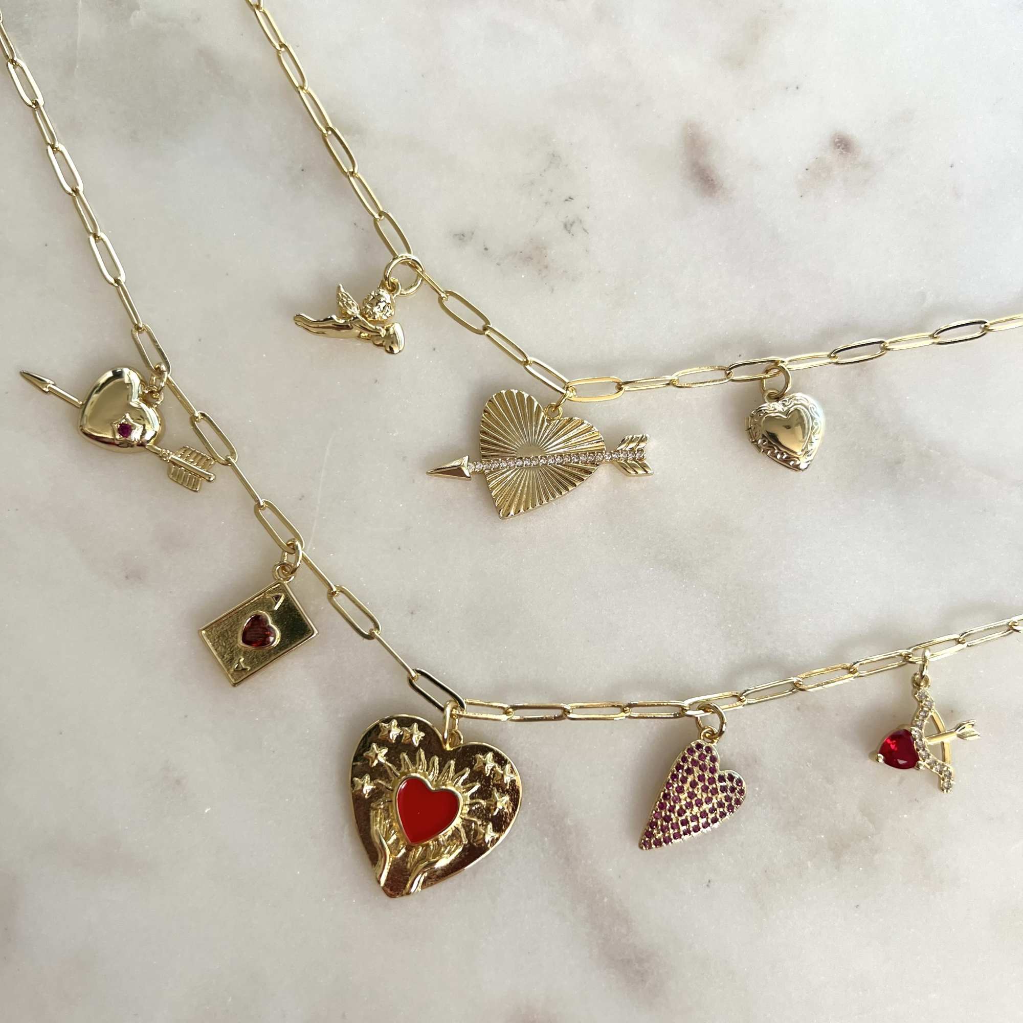 Gold charm necklaces with heart and arrow pendants on a marble surface