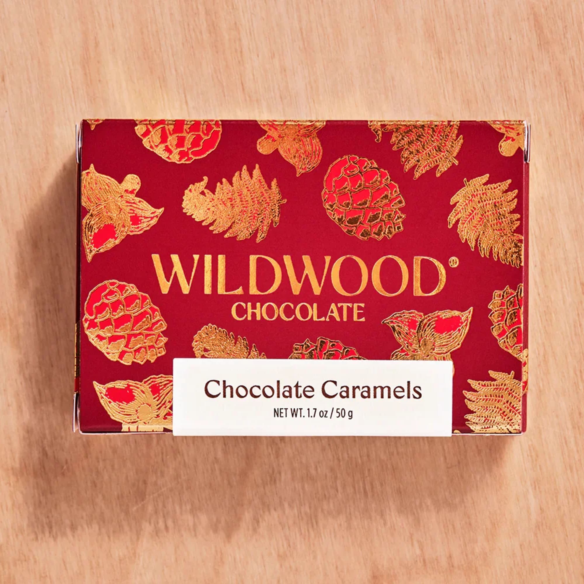 Red box of Wildwood Chocolate Caramels with gold pinecone designs on a wood surface