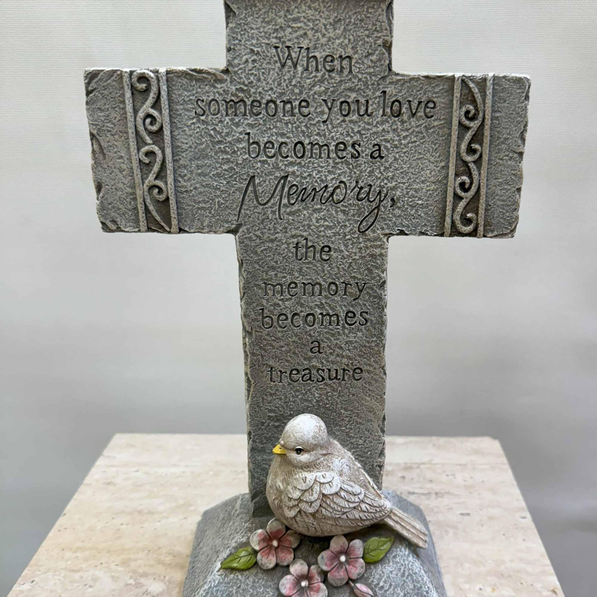 Stone memorial cross with a bird and flowers at the base
